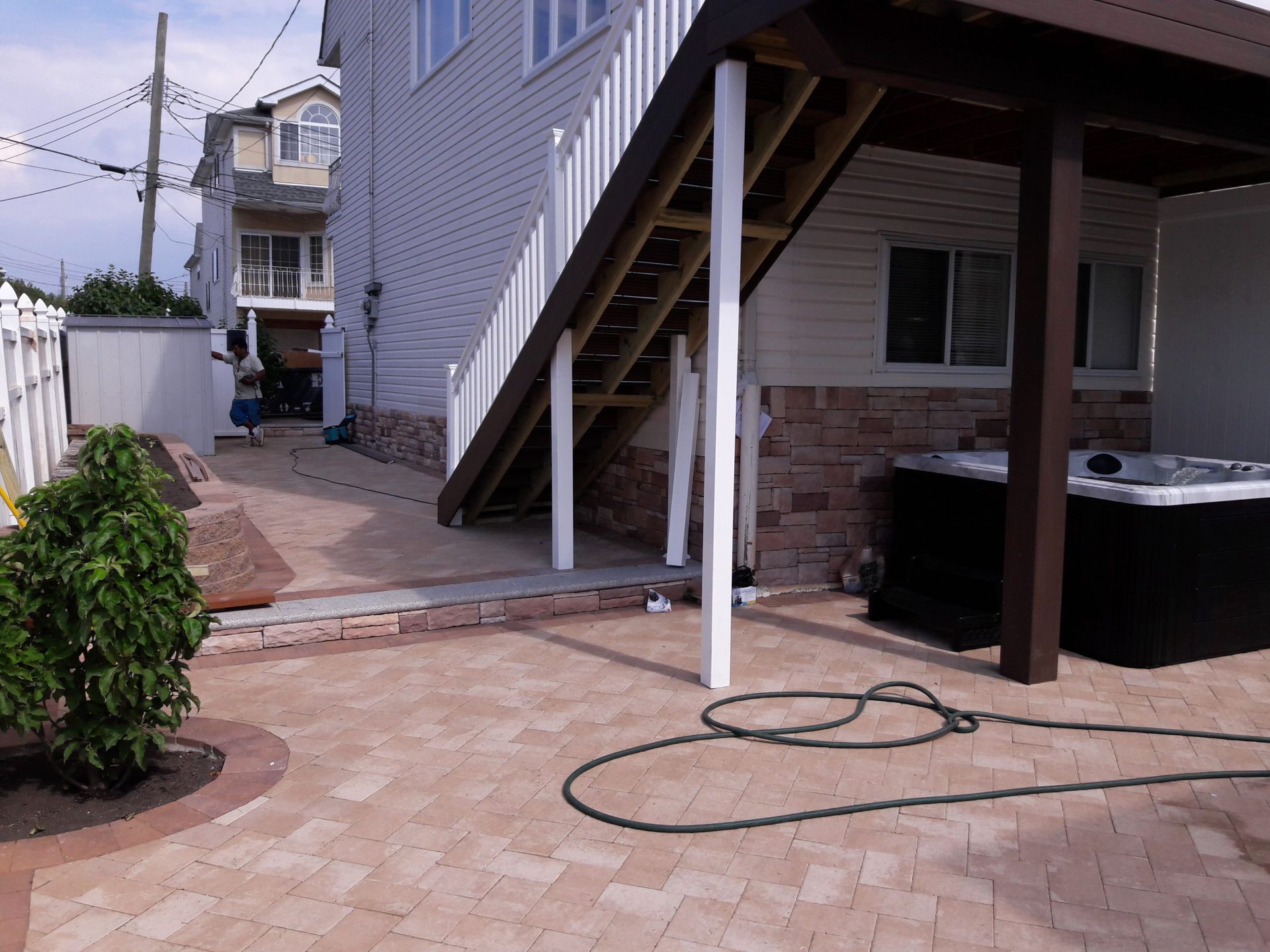 Brick patio with stairs leading to a house. Hot tub sits under a deck.