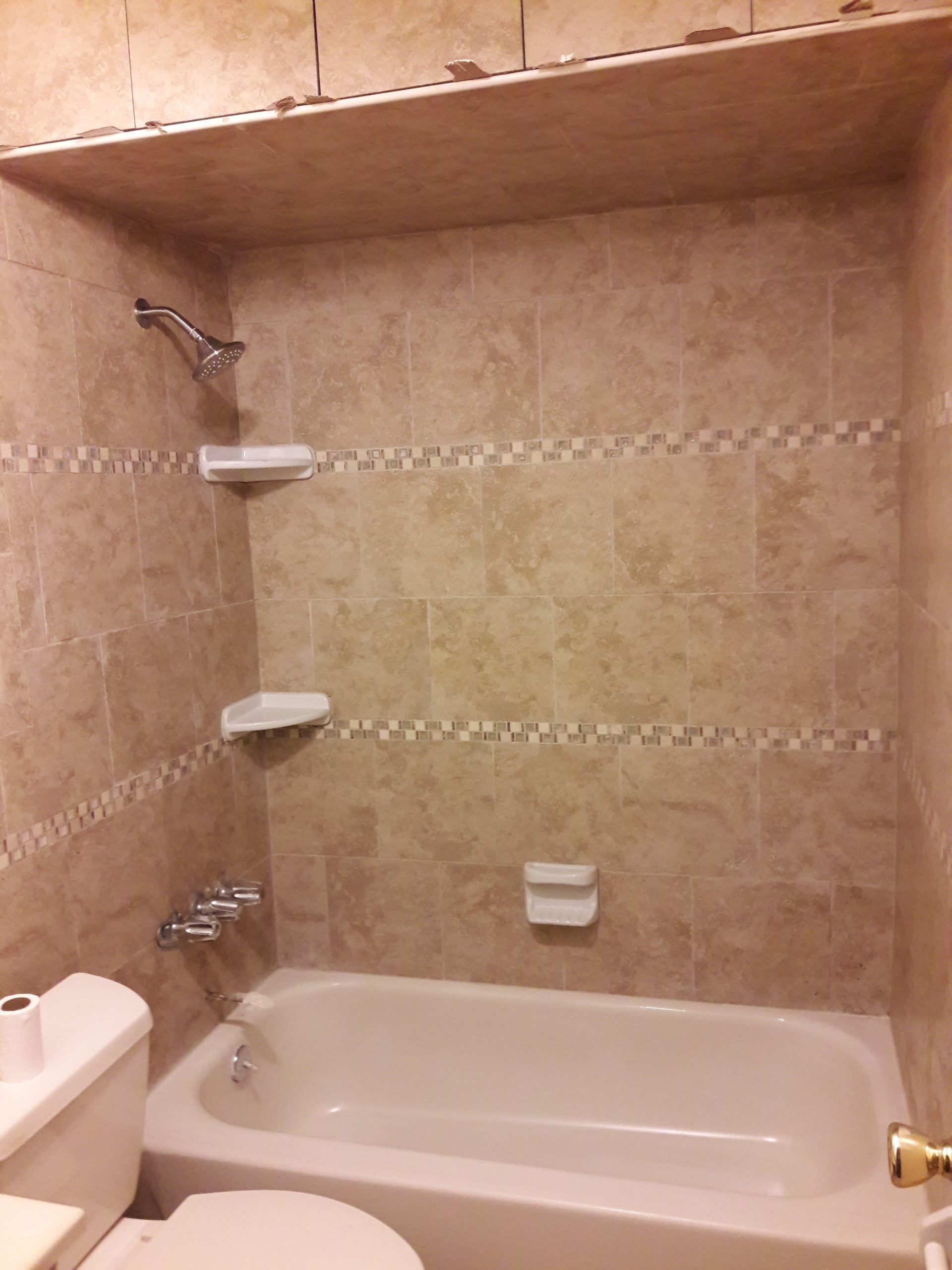 Tiled bathroom with a bathtub, toilet, and showerhead. Beige and cream tones.
