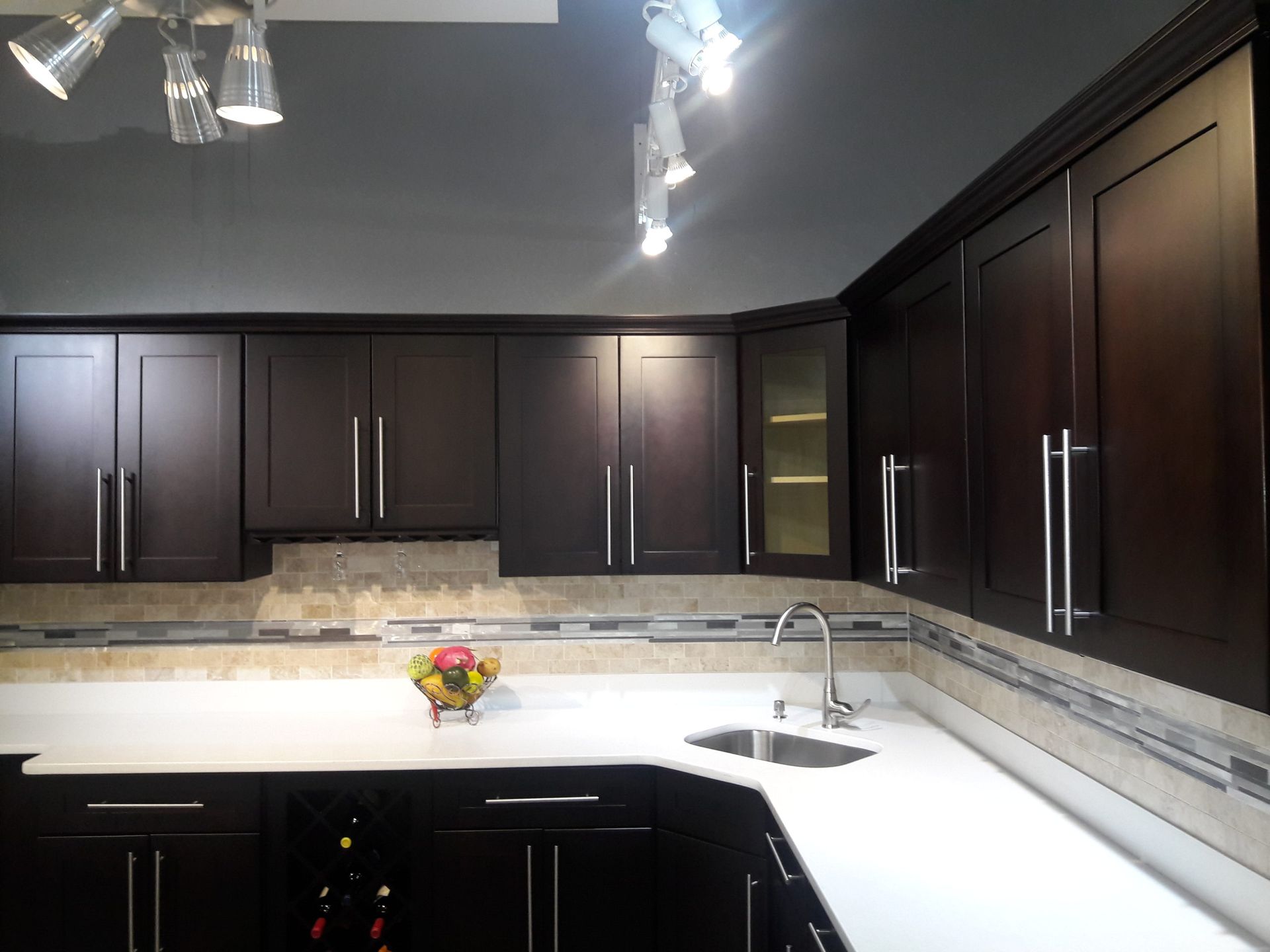 Dark brown kitchen cabinets with white countertops, sink, and track lighting.