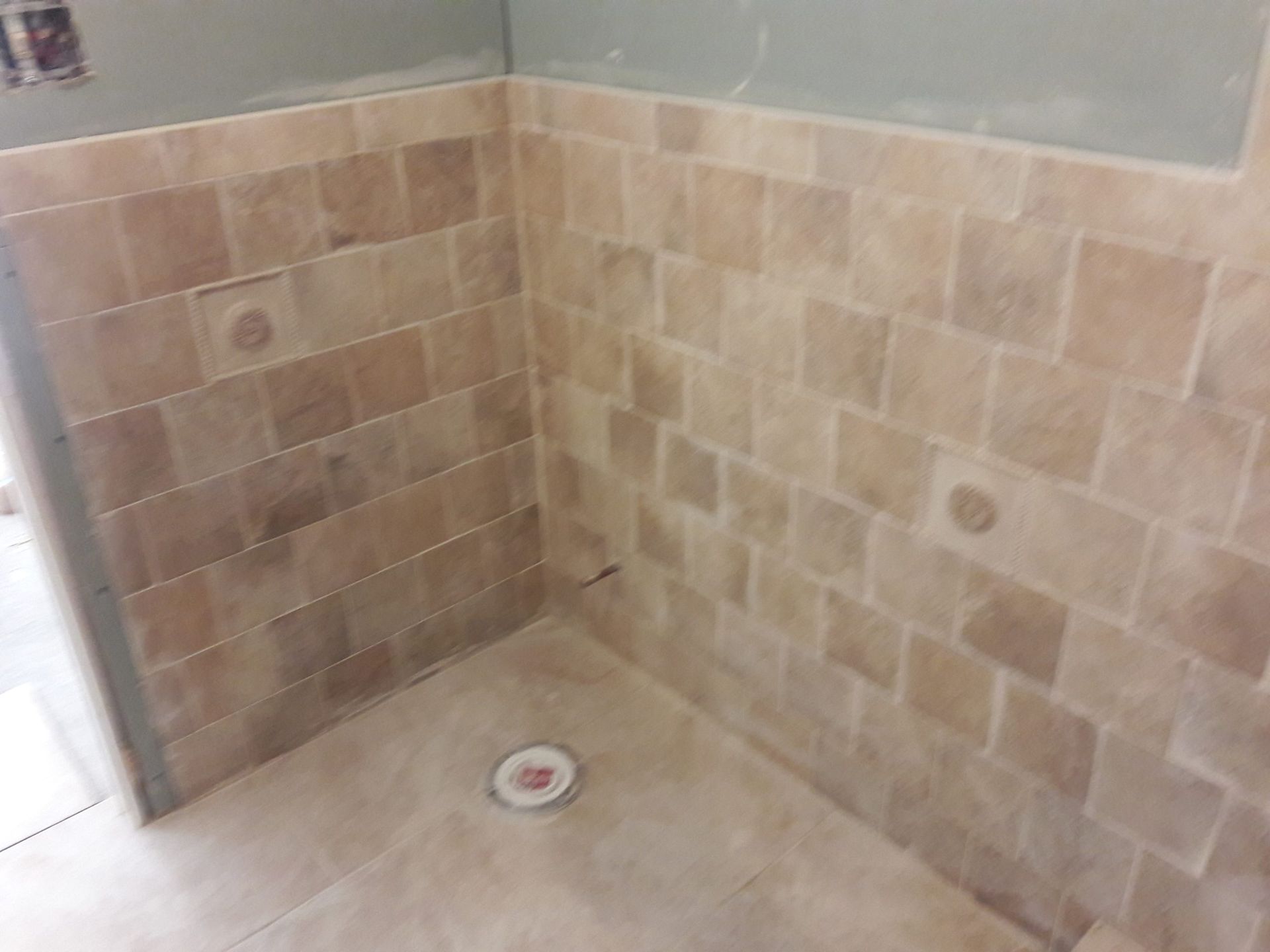 A partially tiled shower enclosure with beige tiles and a floor drain, under construction.