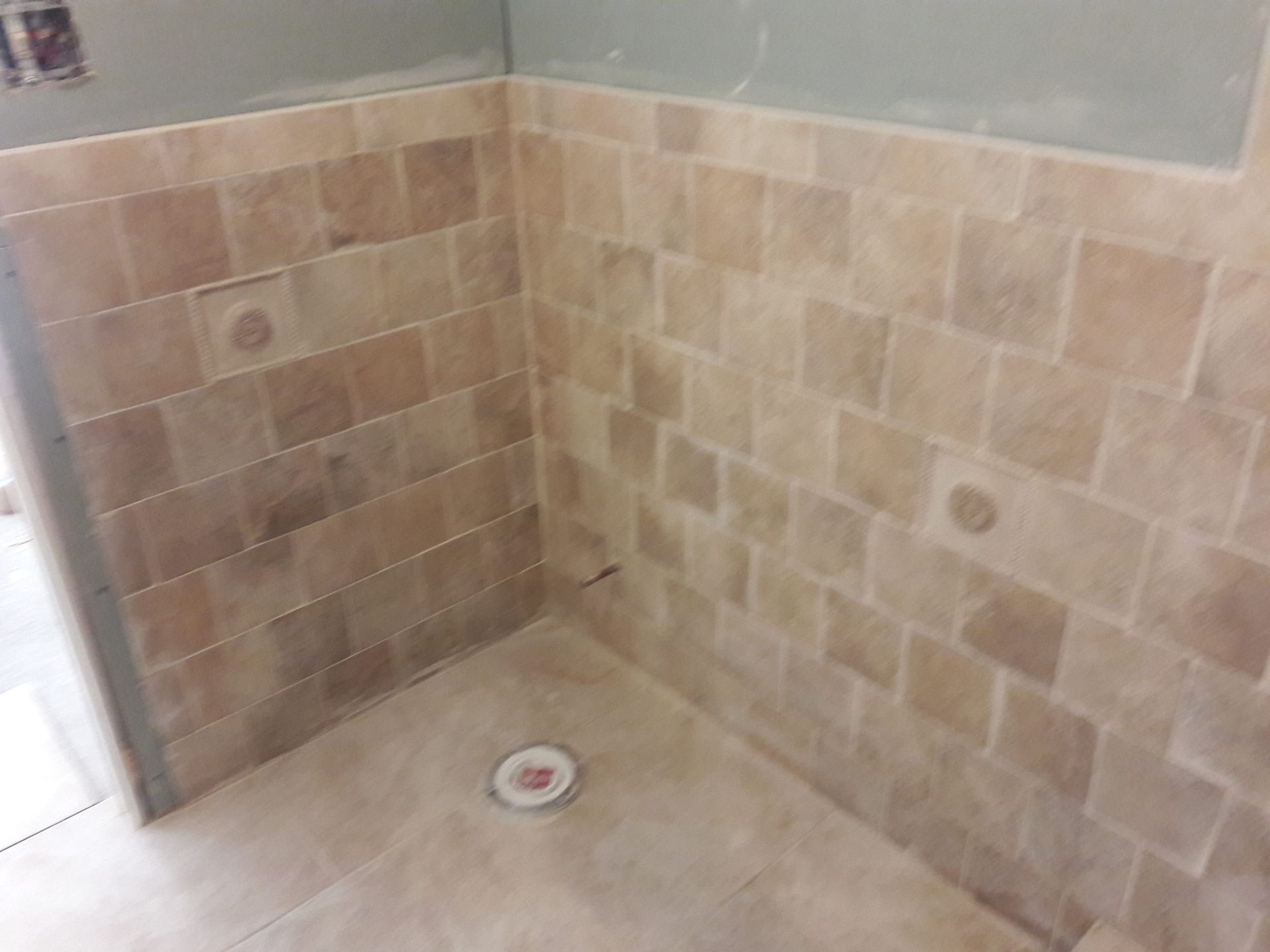 Tiled shower stall with beige tiles. Drain in the floor, holes in the walls.