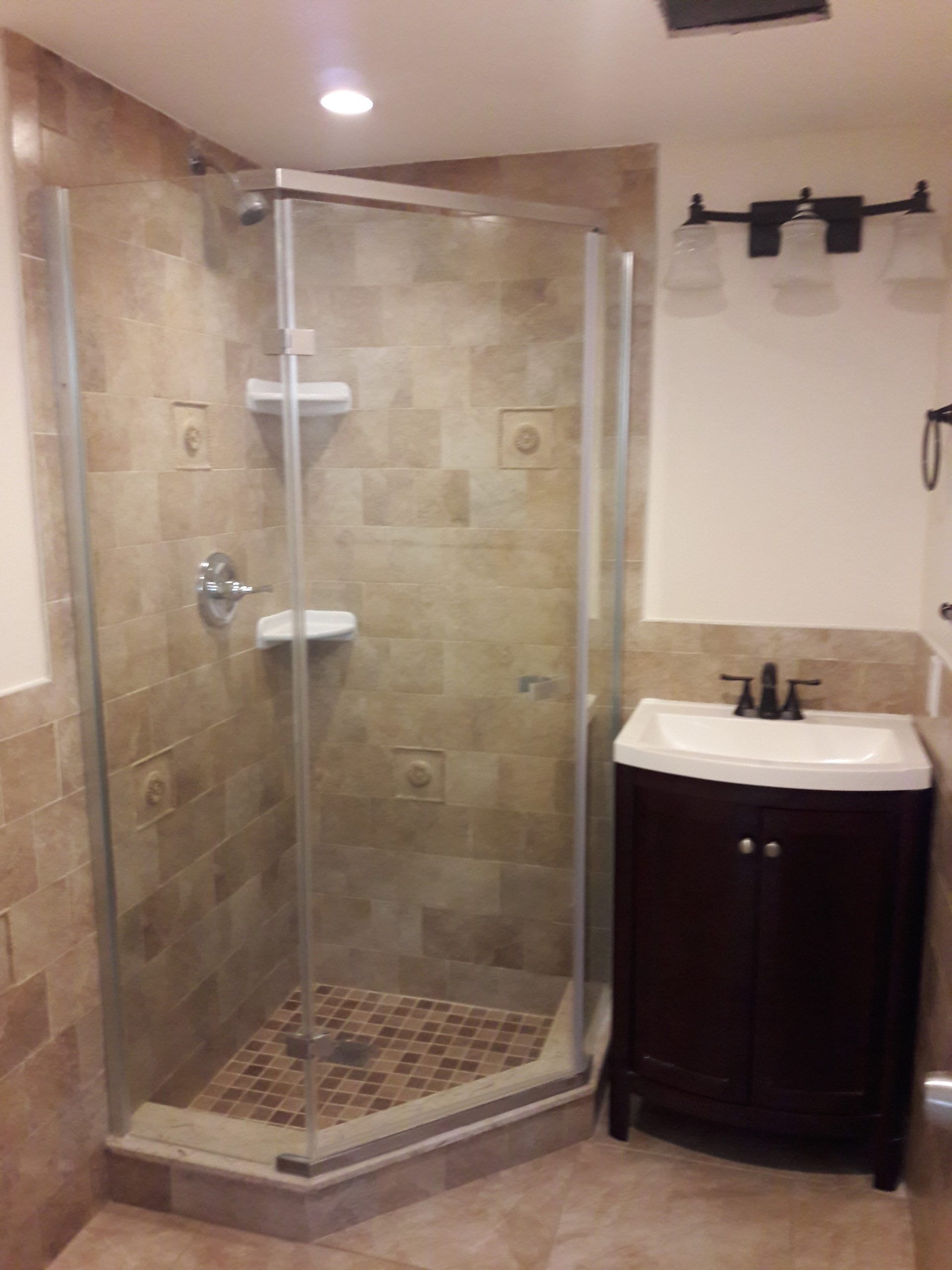 Bathroom with tile shower, glass door, dark vanity, and bronze fixtures.