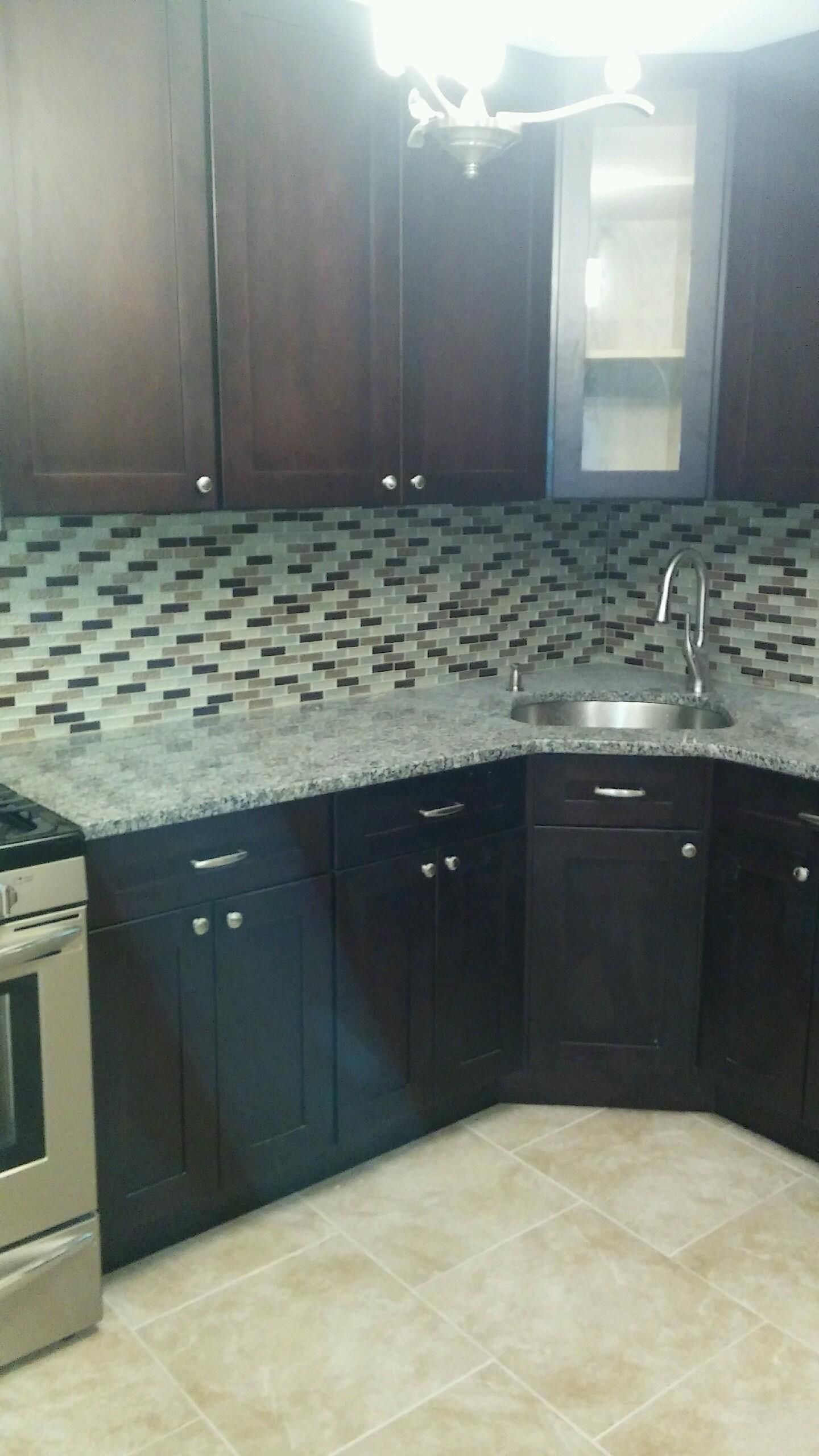 Kitchen with dark cabinets, granite countertop, tiled backsplash, stainless steel sink and appliances.