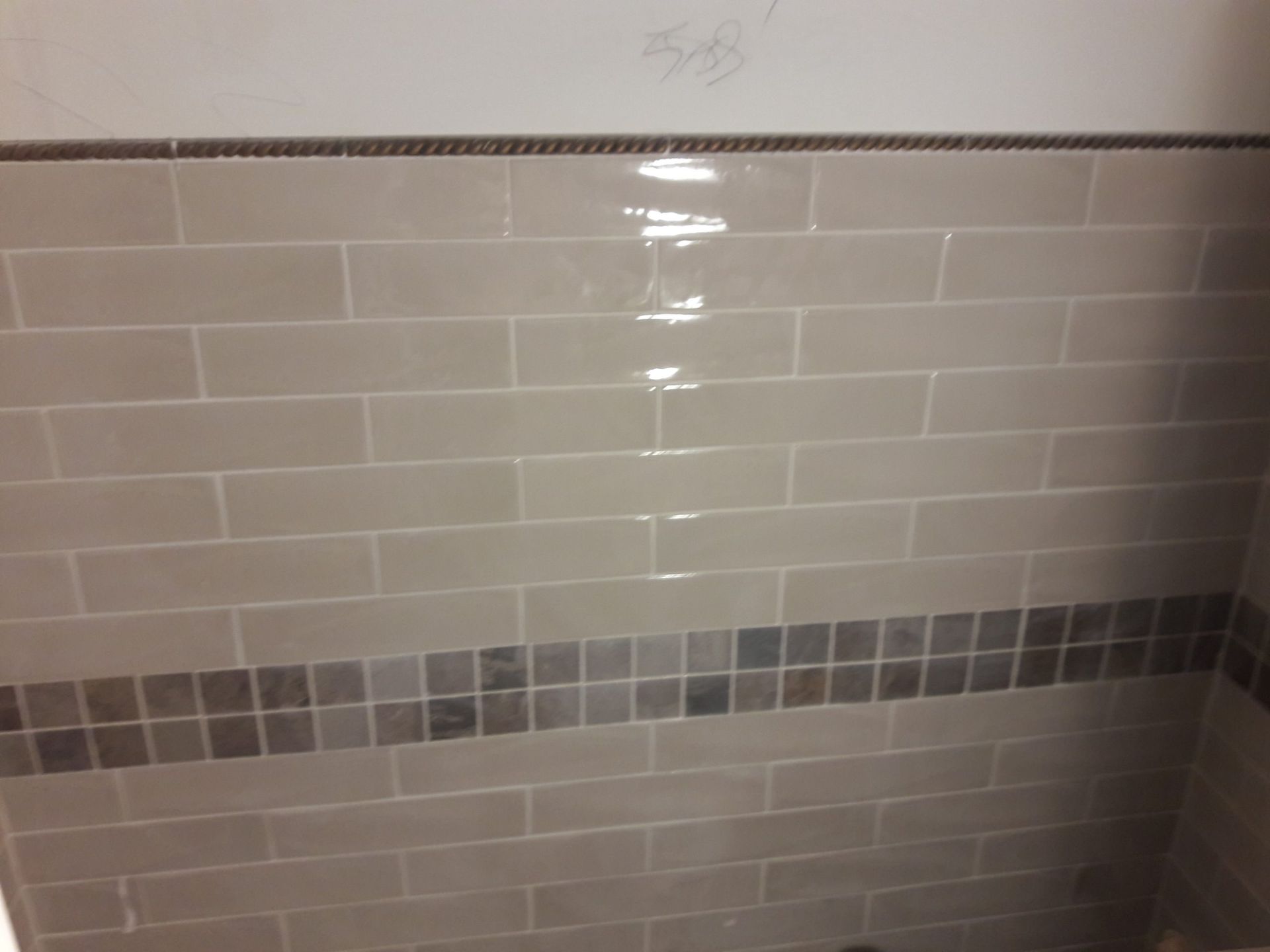 Beige rectangular tiles on a bathroom wall with a dark tile border. The wall is wet.