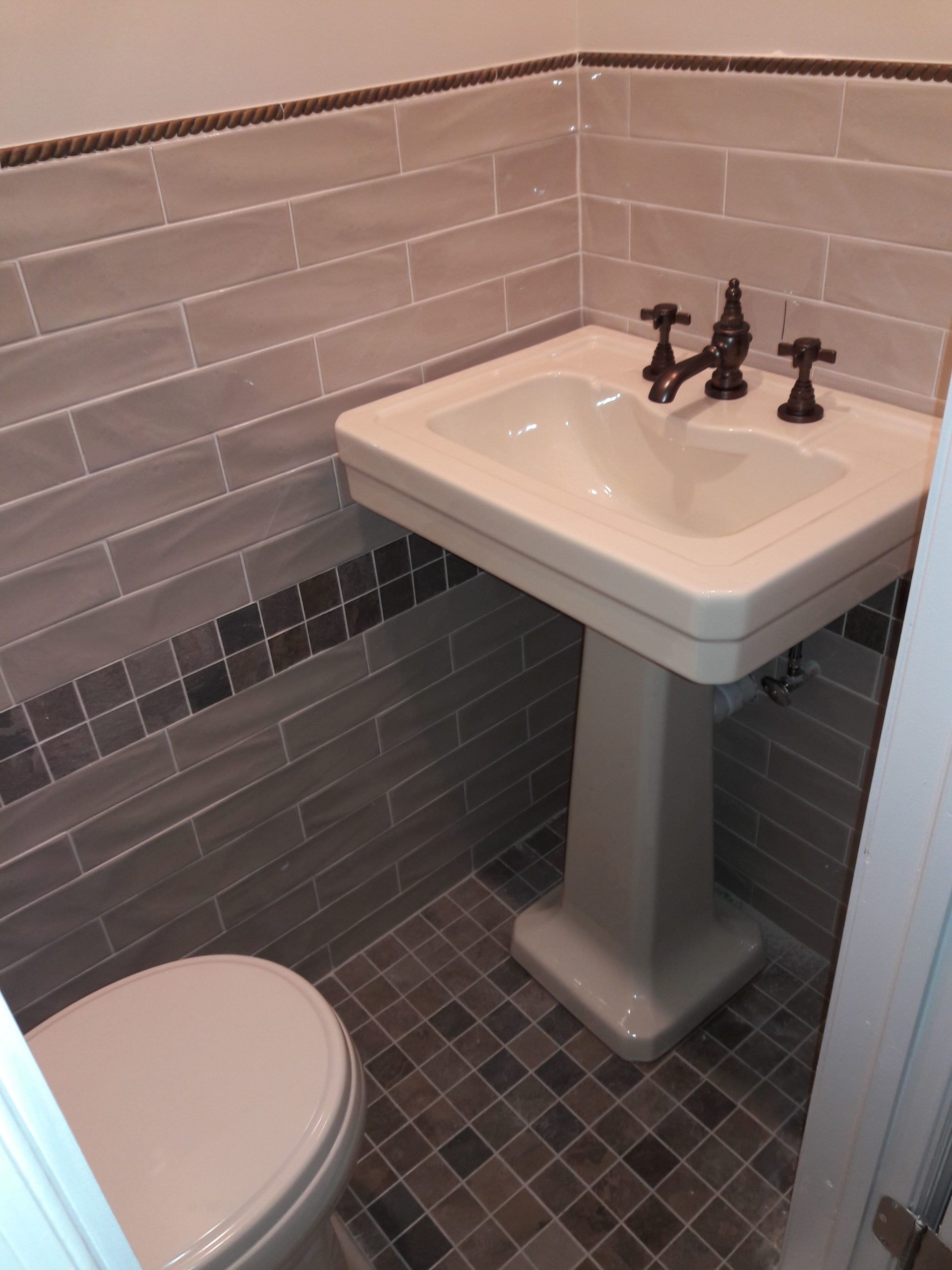 Pedestal sink in a small bathroom with gray tile walls and floor.