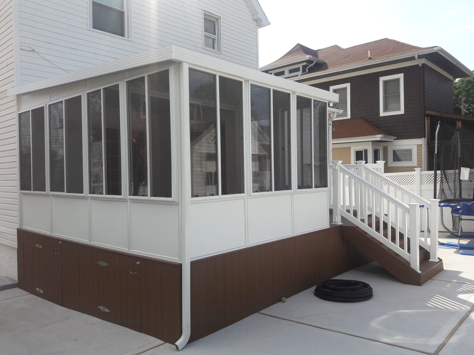 White and brown screened-in porch attached to a house with a small deck and stairs, outside.