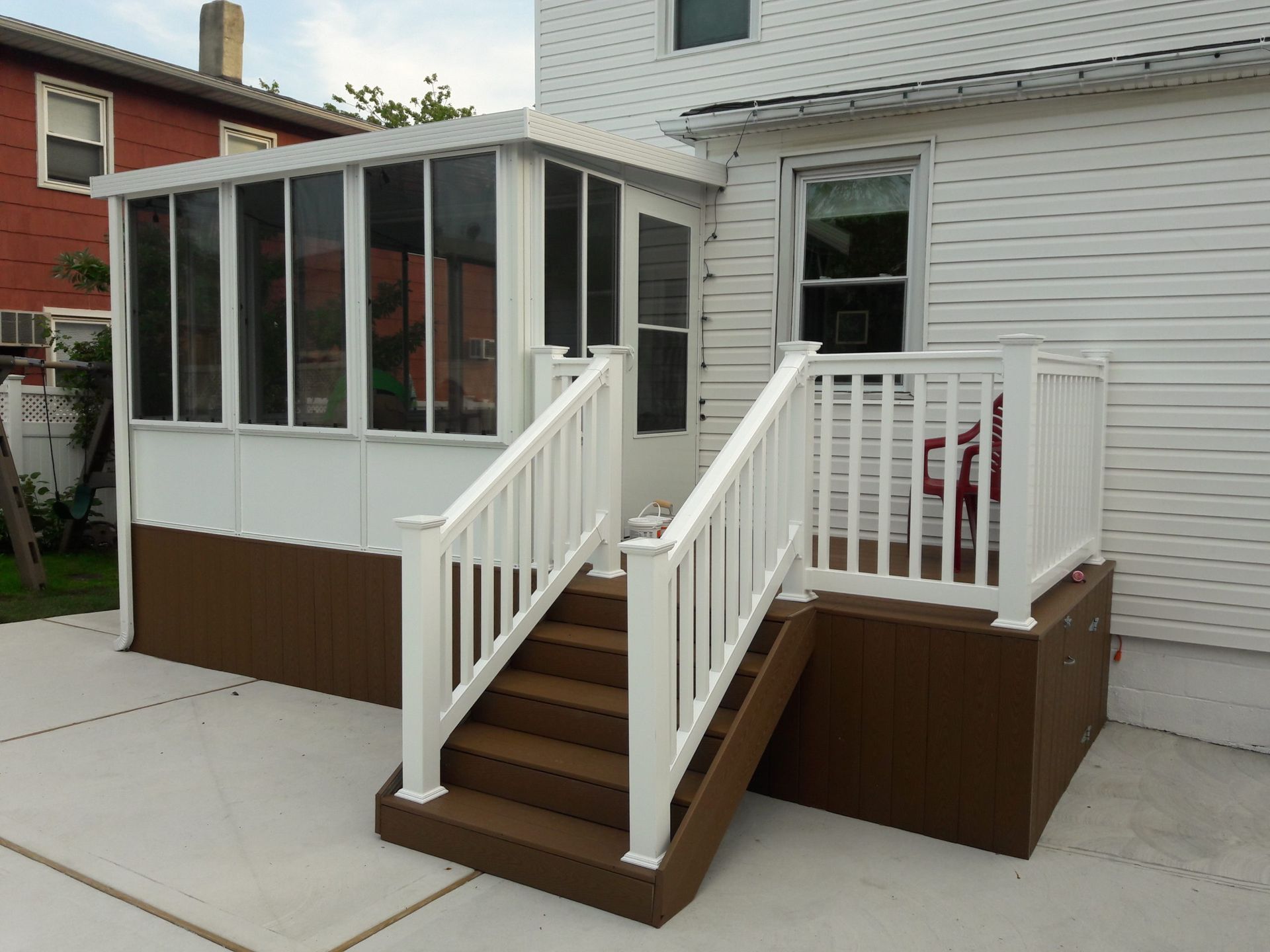 White porch with stairs and railing, leading to a screened-in sunroom attached to a white house.