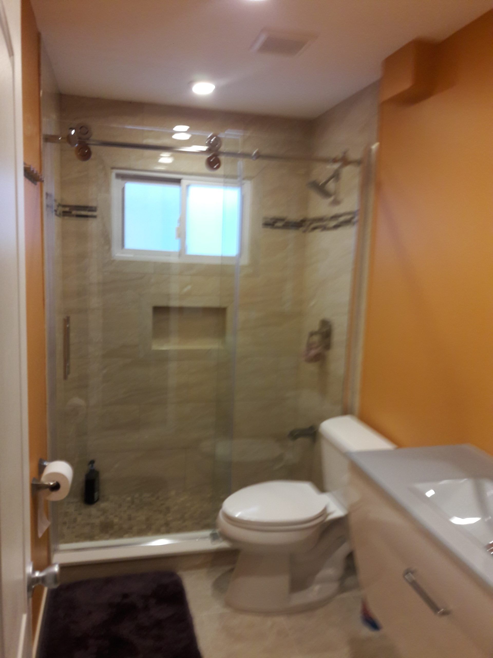 Bathroom with glass shower, toilet, sink, and orange wall.