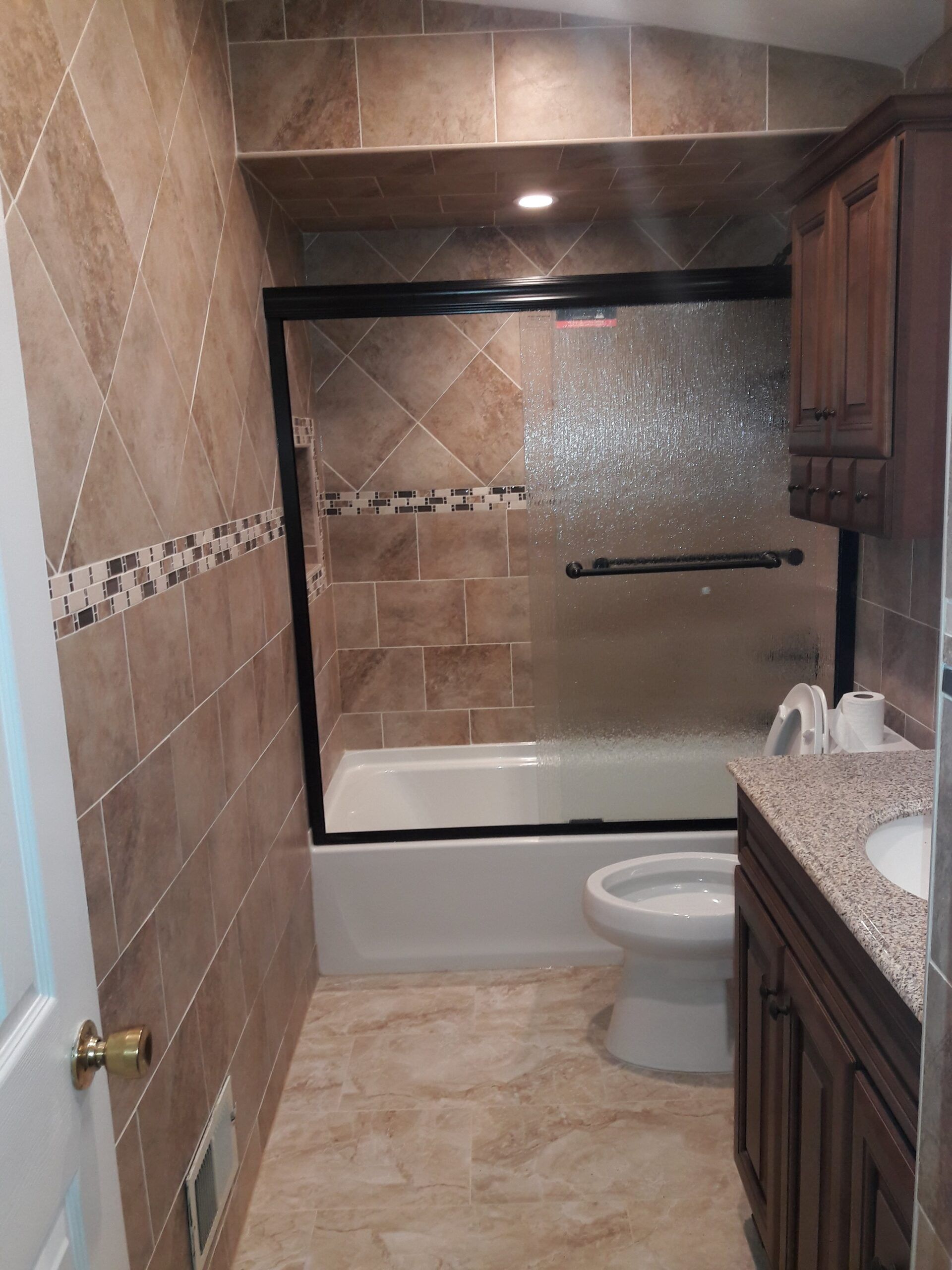 Bathroom with brown tile walls, a white tub, toilet, and dark wood vanity with a granite countertop.