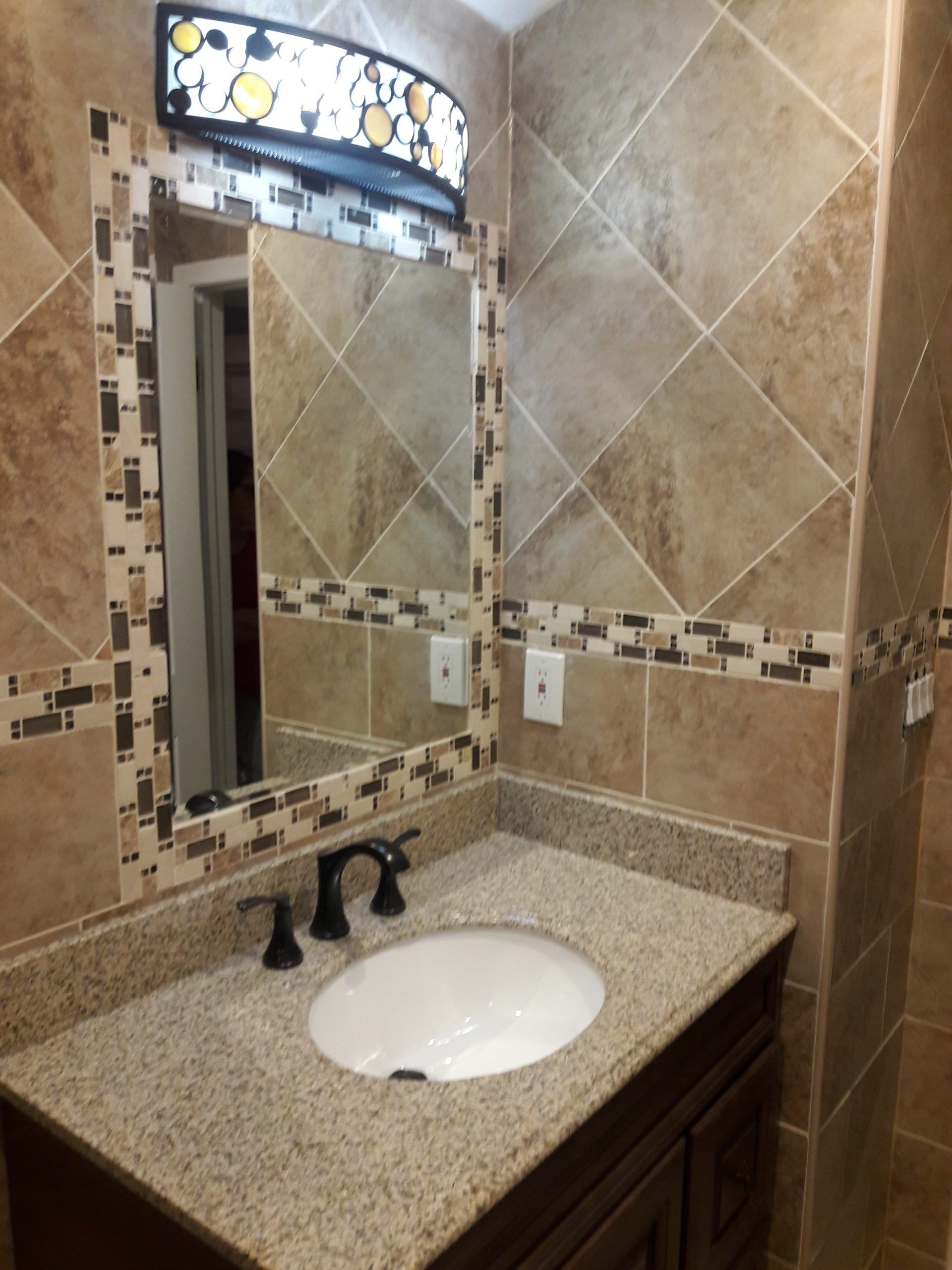 Bathroom with tan tile walls, granite countertop, oval sink, and a decorative mirror frame.