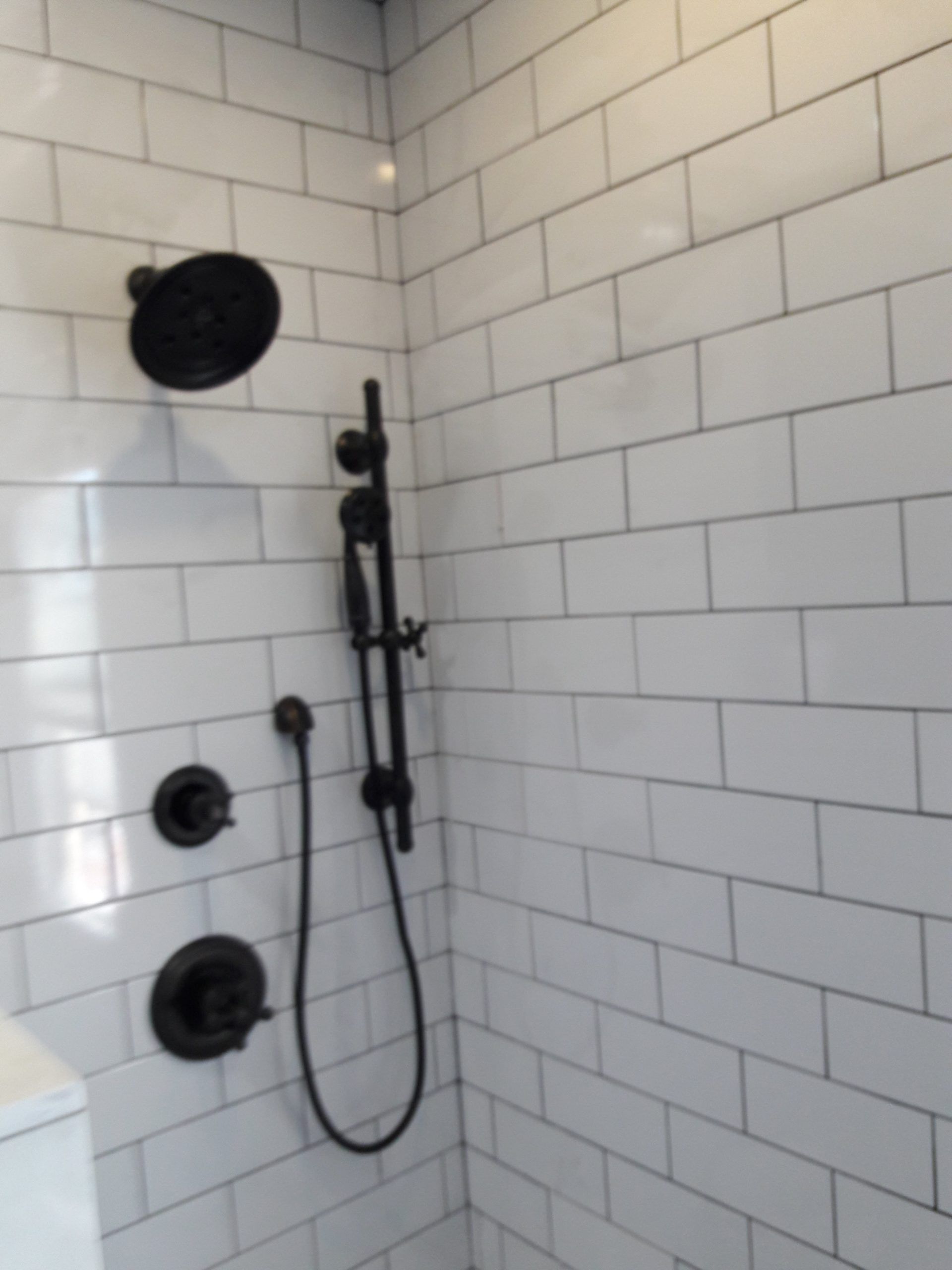 Black shower fixtures on white subway tile in a bathroom.