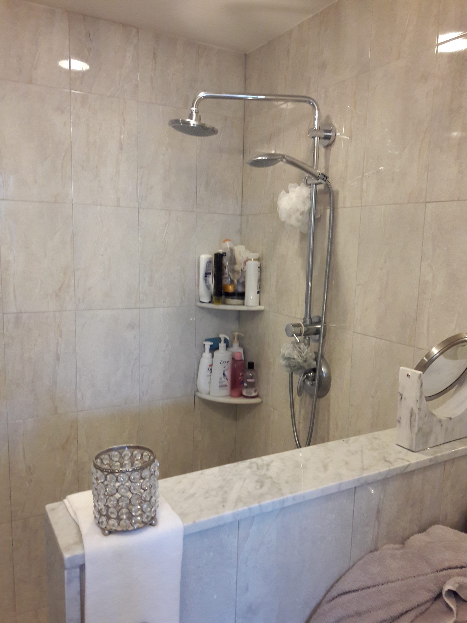 Shower with a marble ledge, tiled walls, and two shower heads. Corner shelves hold toiletries.