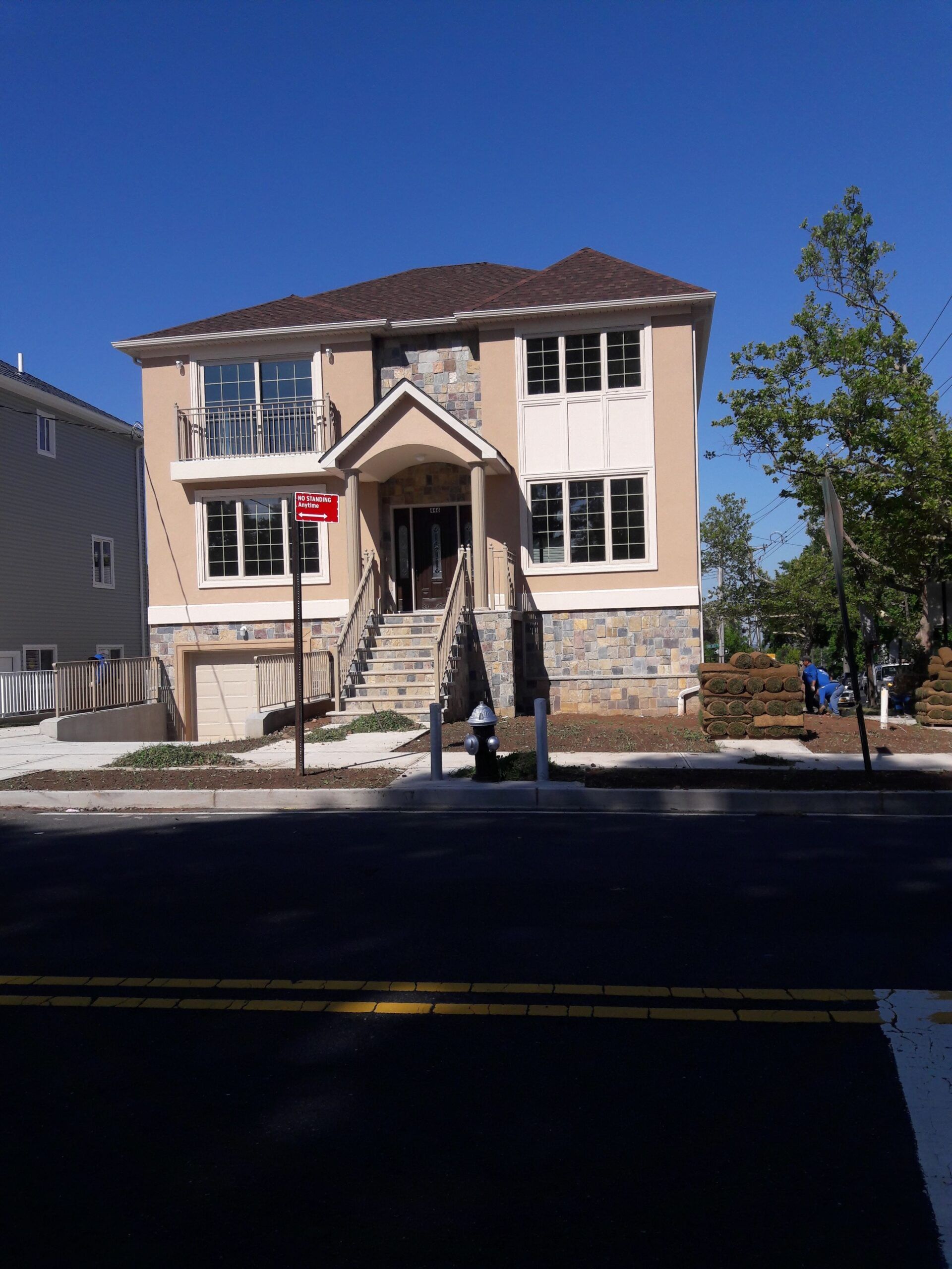 Two-story beige house with stone accents, stairs leading to the entrance, blue sky.