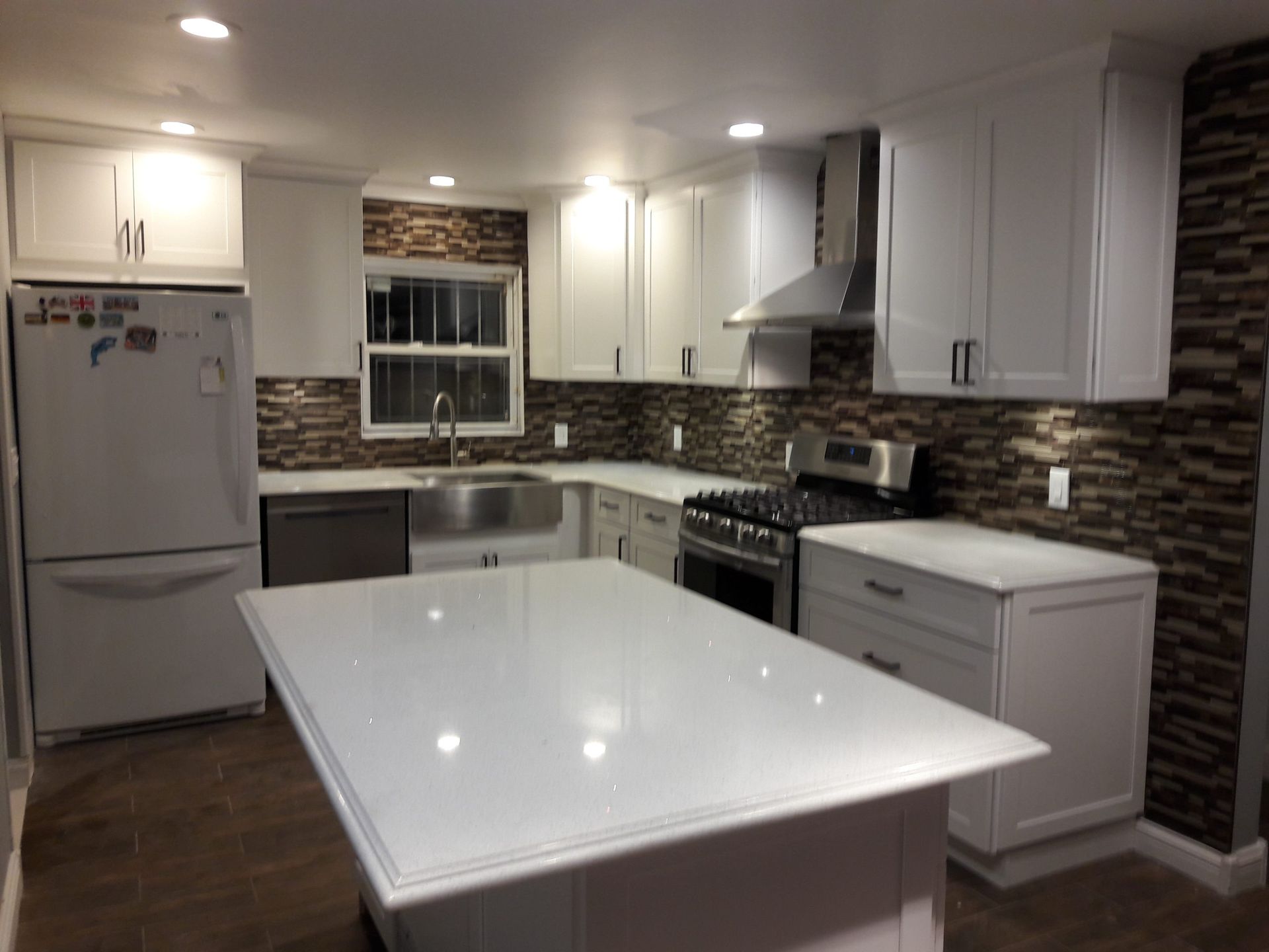 Modern white kitchen with island, stainless steel appliances, and textured backsplash.