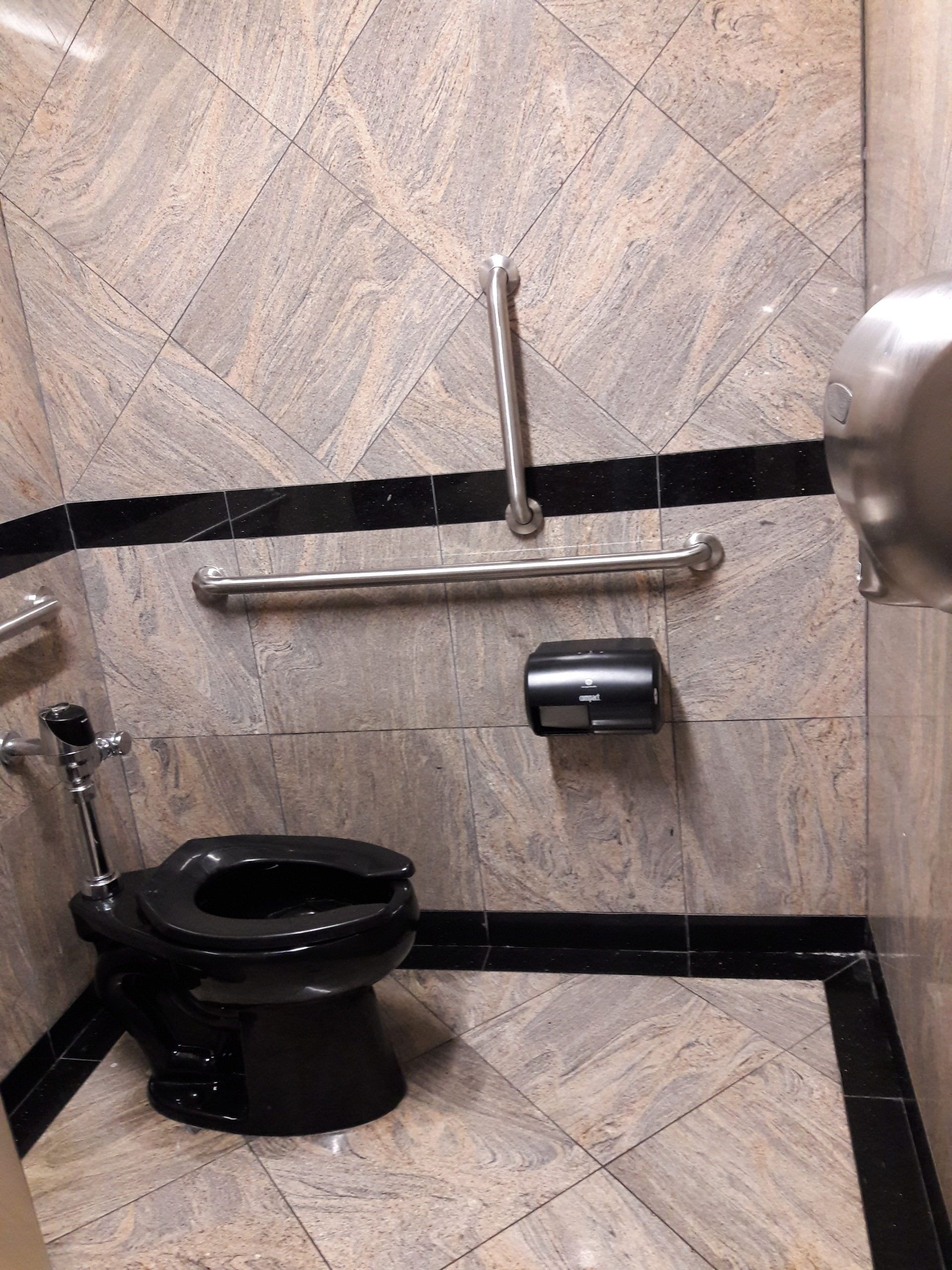 ADA-compliant public restroom with black toilet, grab bars, and black tile accents.