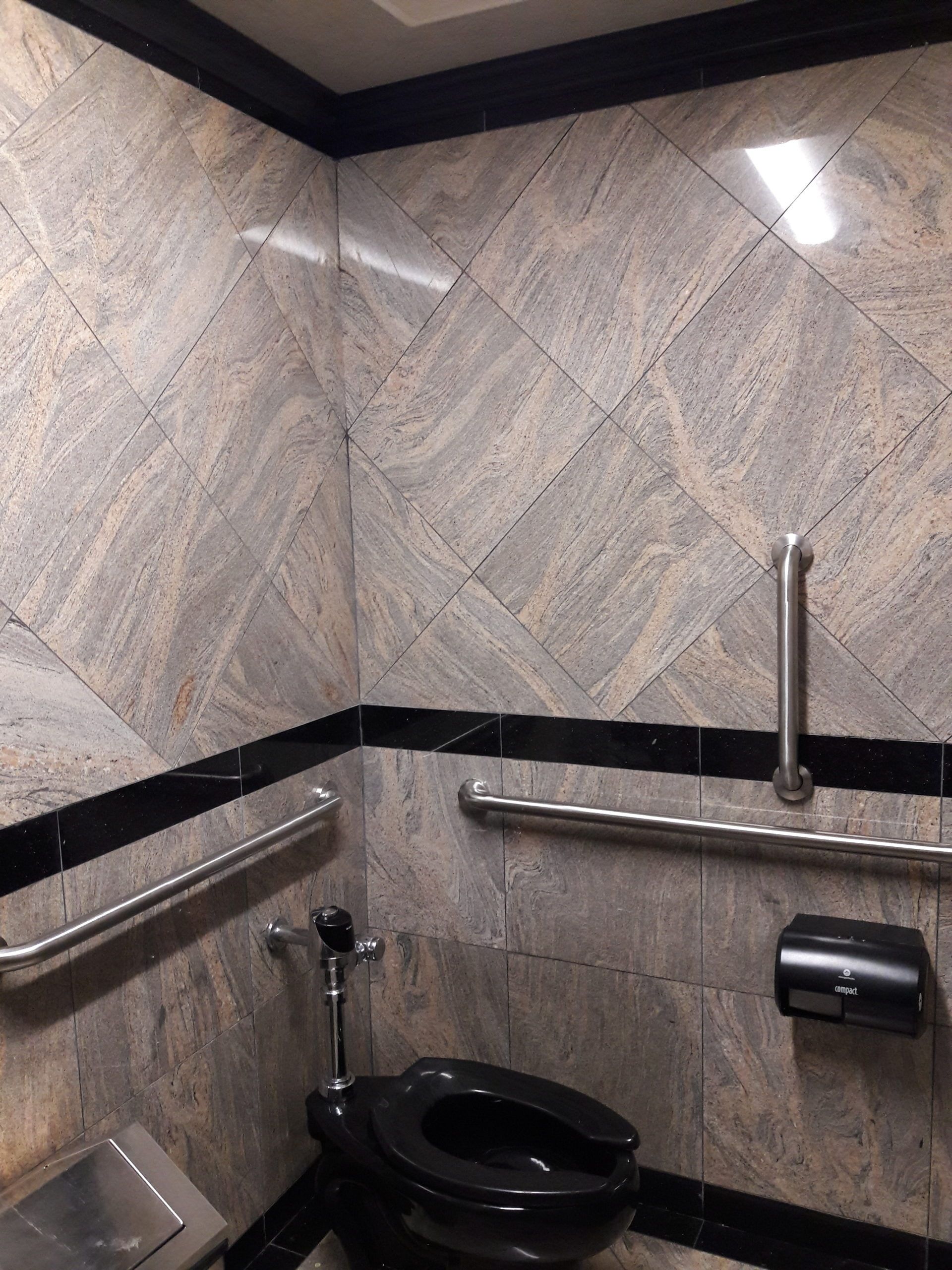 Accessible restroom with black toilet, grab bars, and angled granite tile.