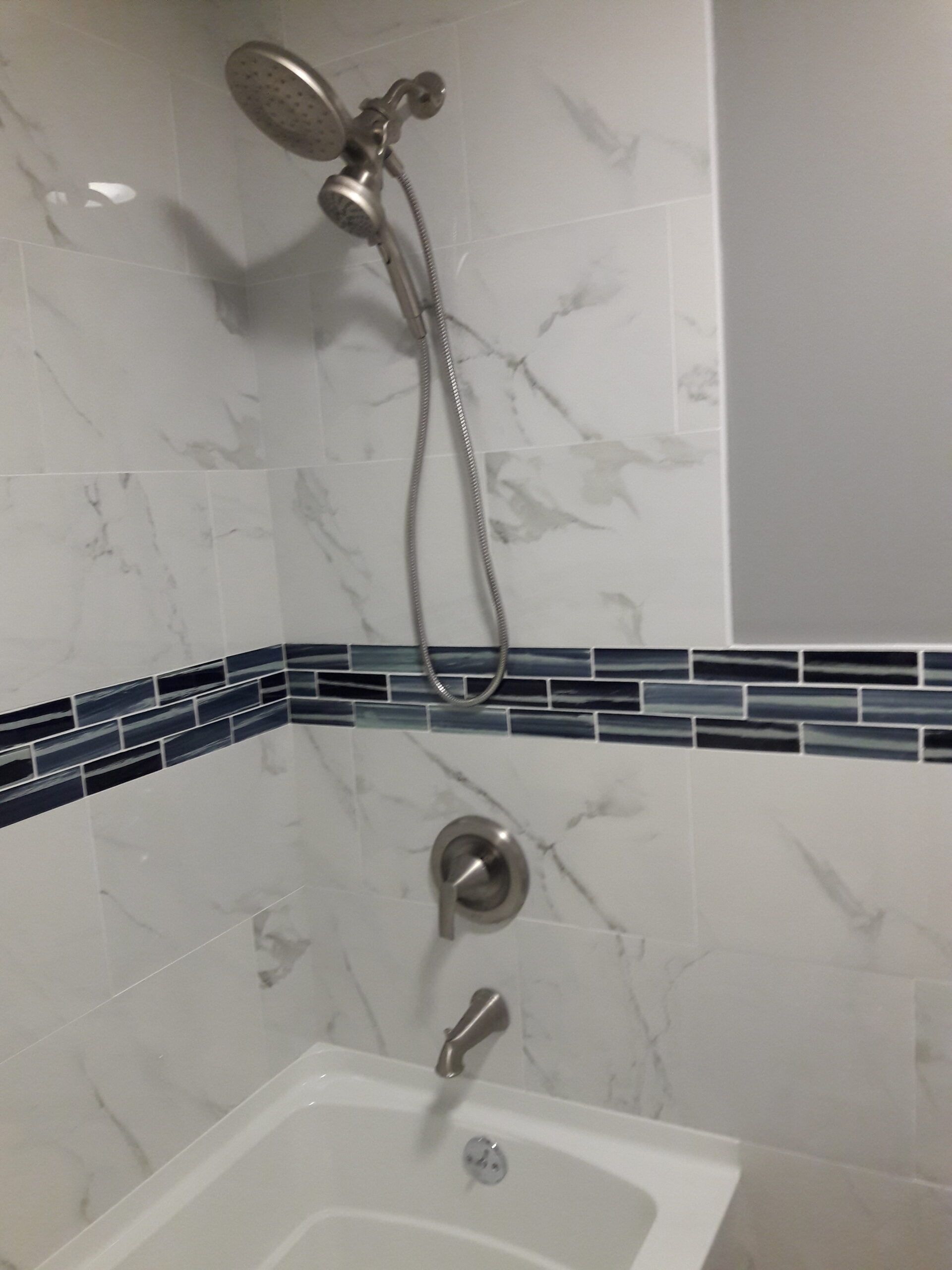 Bathroom shower with white marble-look tiles, blue mosaic accent, and silver fixtures.