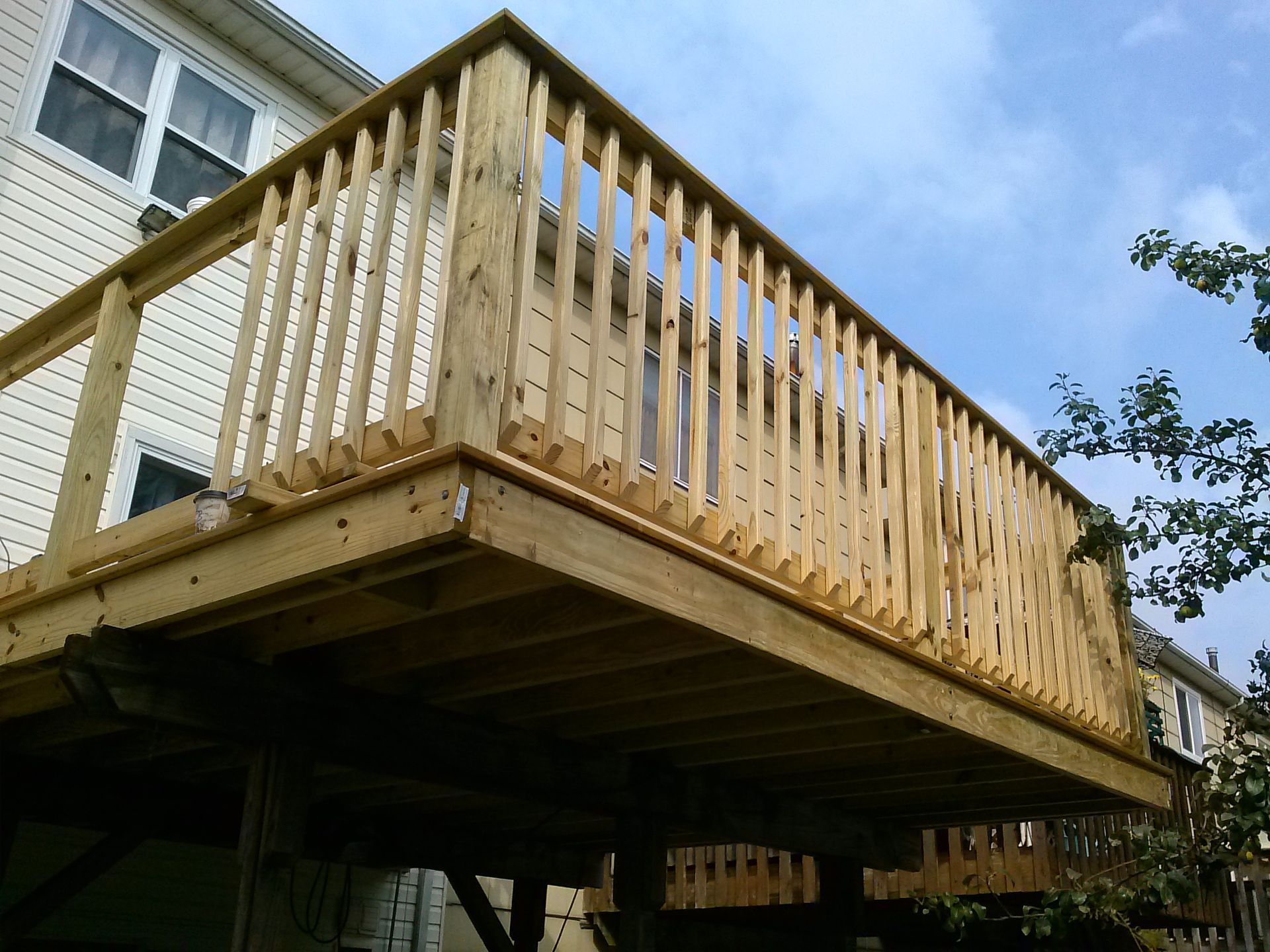 Wooden deck with railing attached to a house. Cloudy sky in the background.