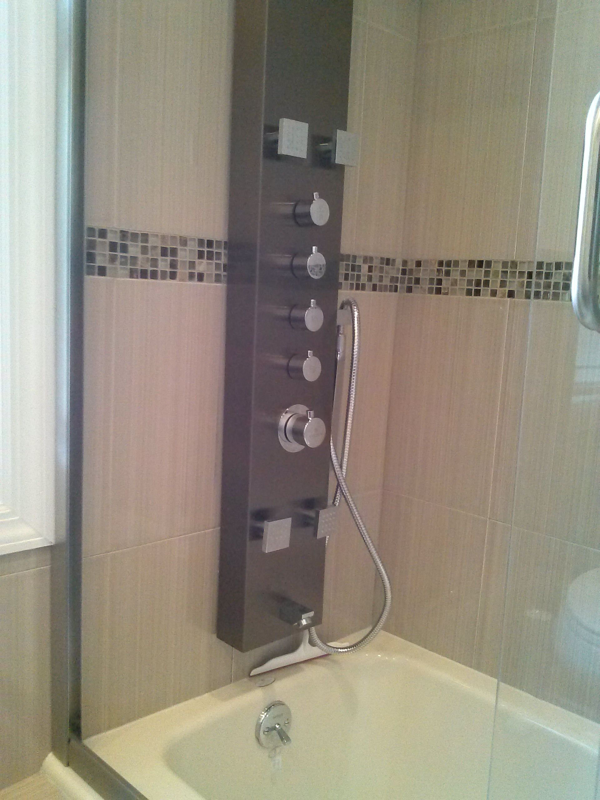 Shower panel with multiple controls and hand shower in a tiled bathroom.