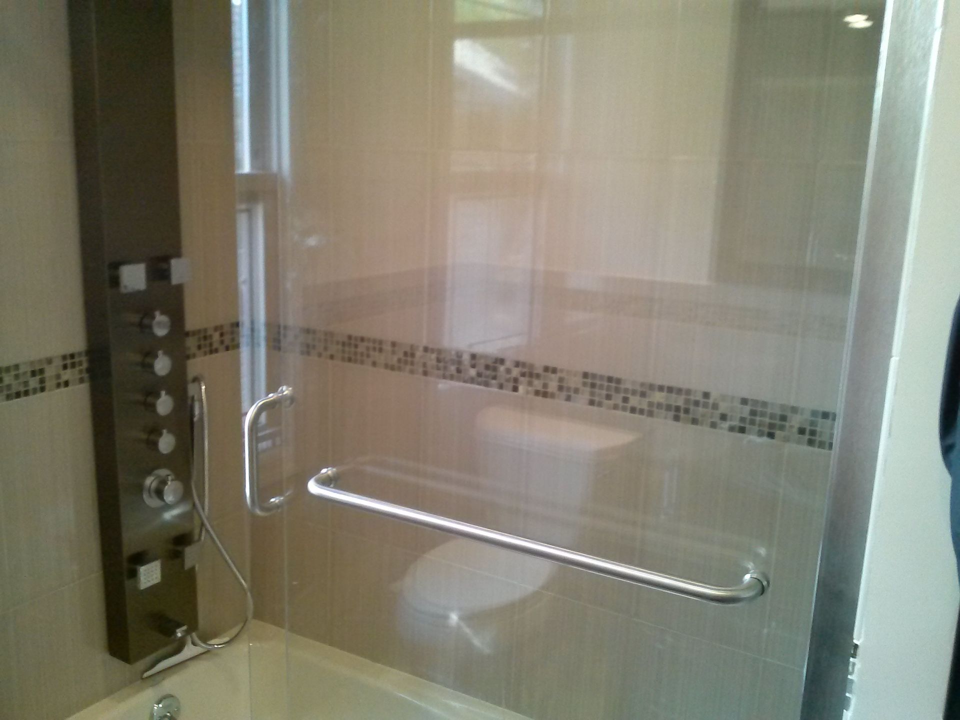 Modern shower stall with glass door, silver fixtures, and tiled walls.