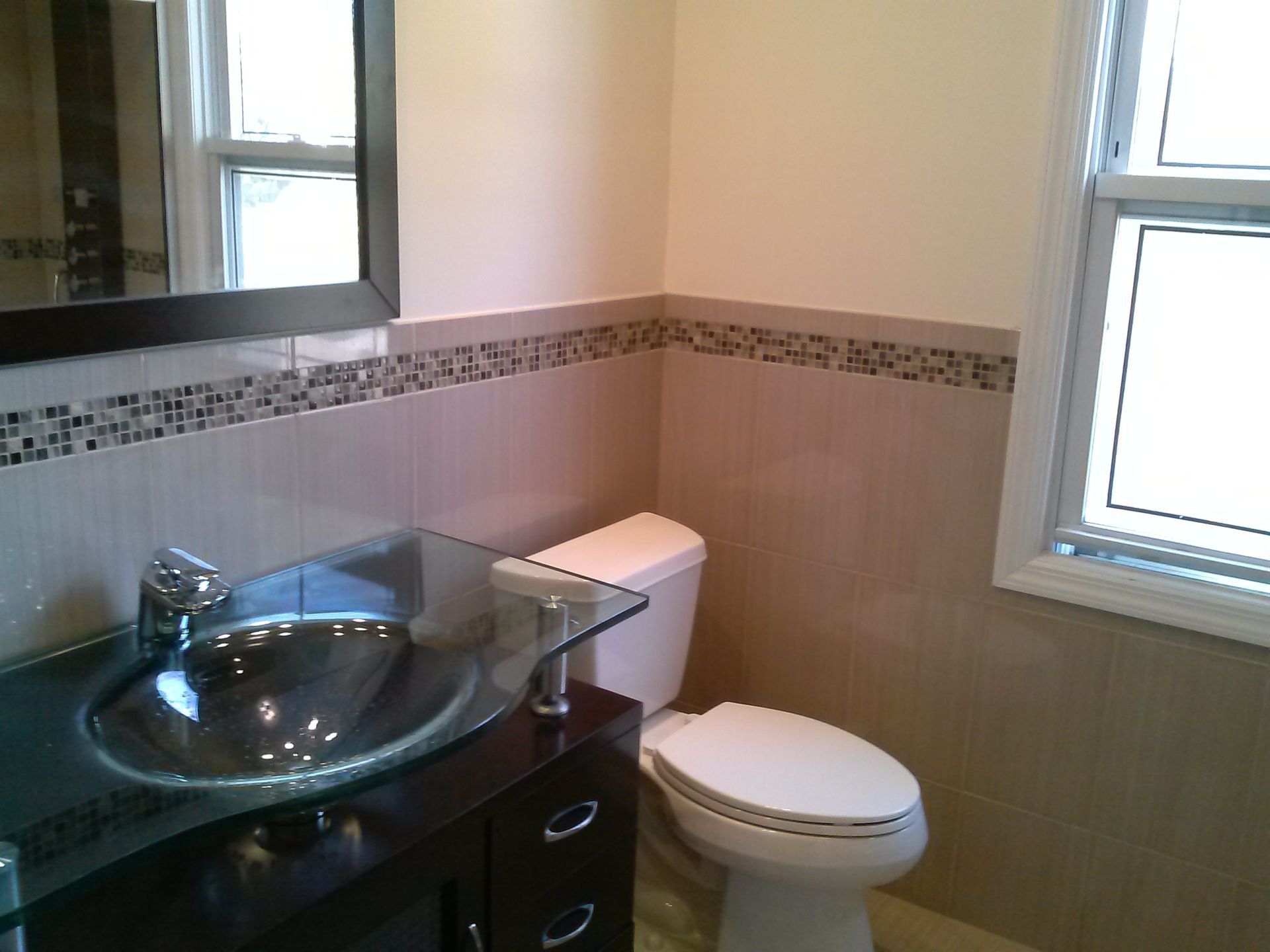 Bathroom with a dark vanity, glass sink, toilet, and beige tile with a decorative tile border.