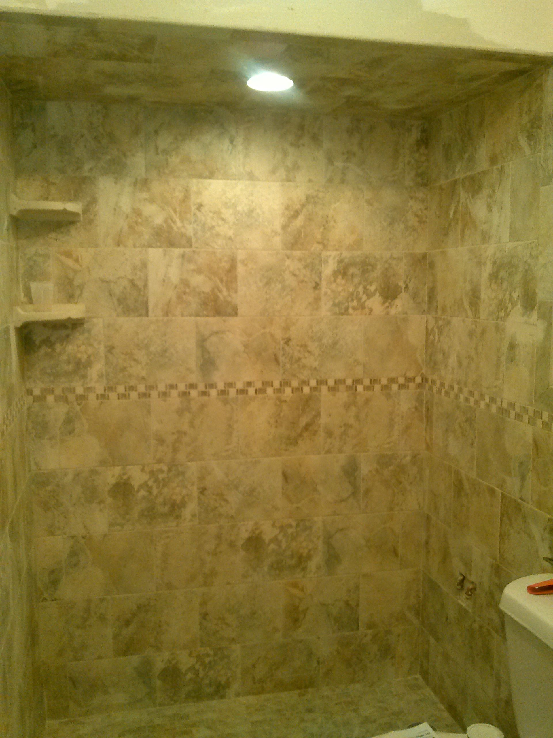 Tiled shower with neutral-toned square tiles and decorative border, with two built-in shelves.