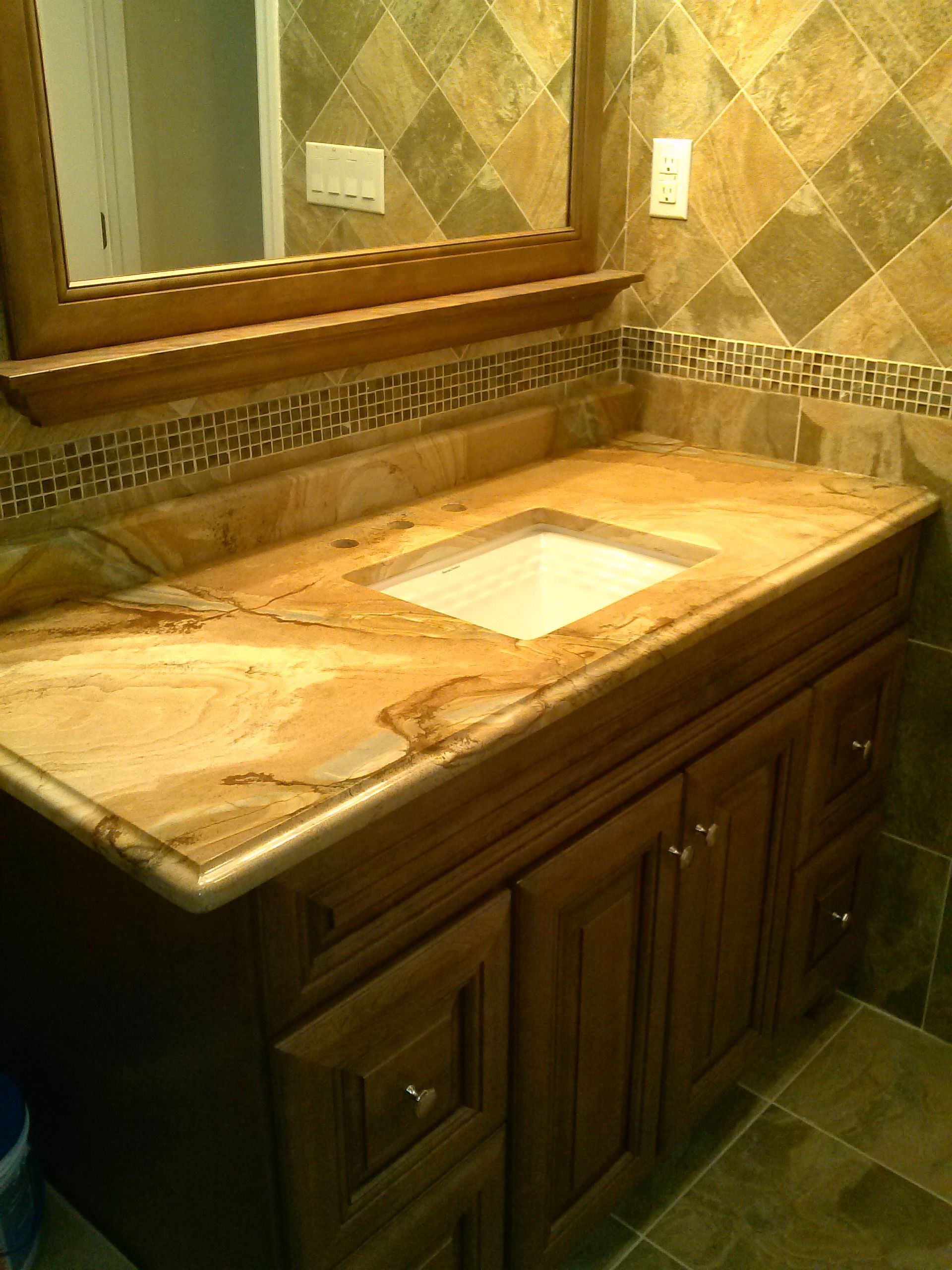 Bathroom vanity with tan granite countertop, wooden cabinets, and decorative tile.