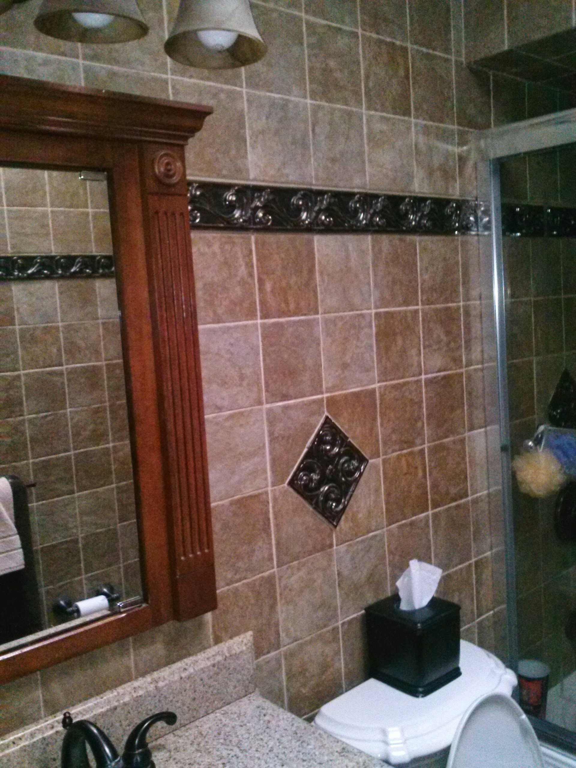 Bathroom with brown tiled walls, wooden framed mirror, and granite countertop.