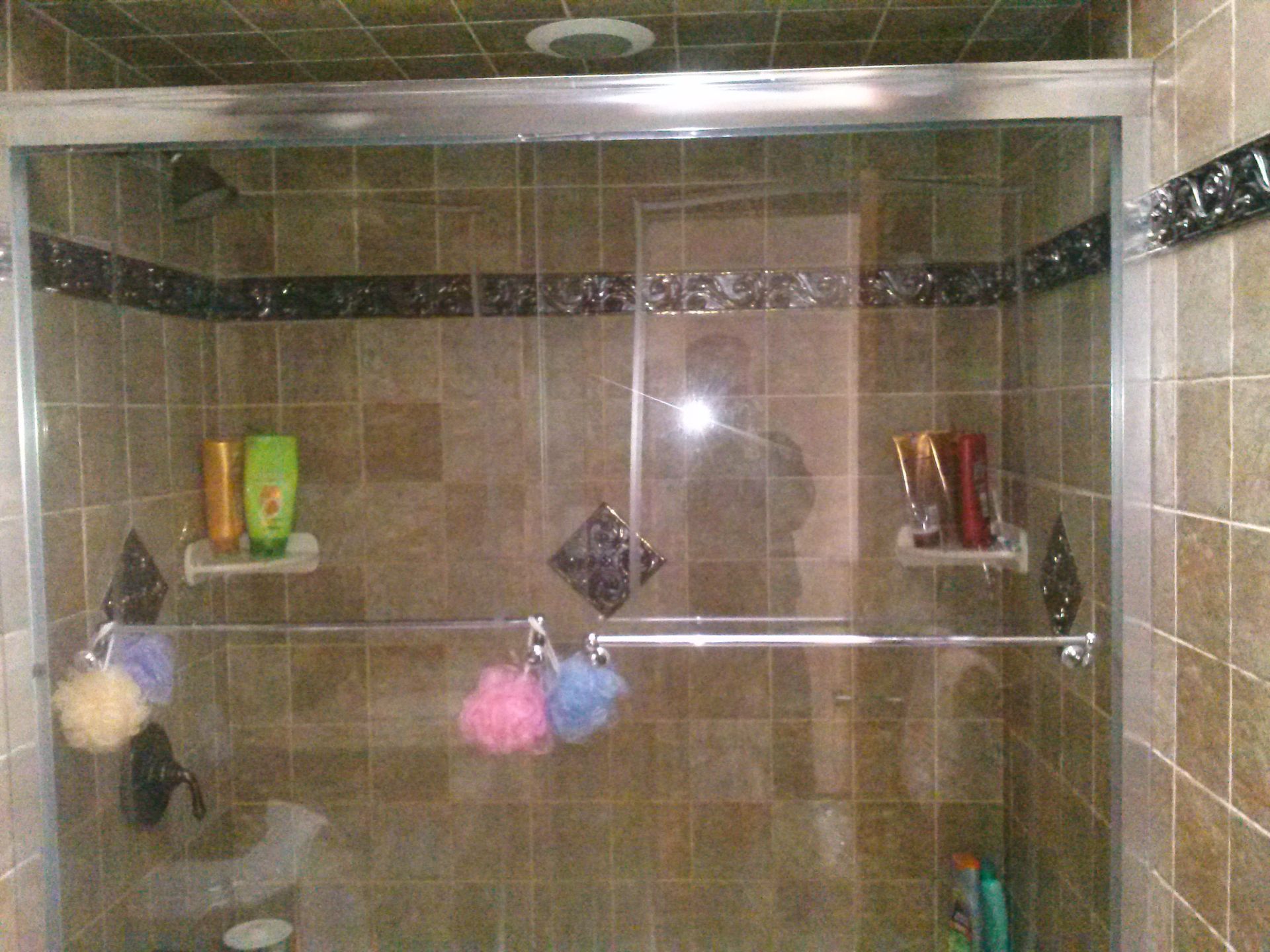 Shower stall with glass doors, brown tile walls, and various toiletries.