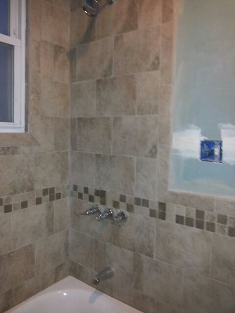 Bathroom with beige tile, small dark mosaic border, window, and unfinished blue alcove.