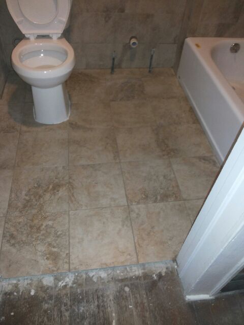 Bathroom with toilet, tub, and tile floor. Brown and beige tile, white toilet and tub, light brown walls.