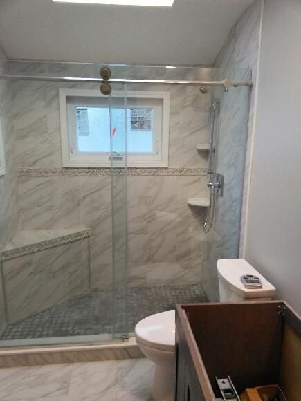 Bathroom with marble tile shower, glass door, toilet, and wooden vanity.