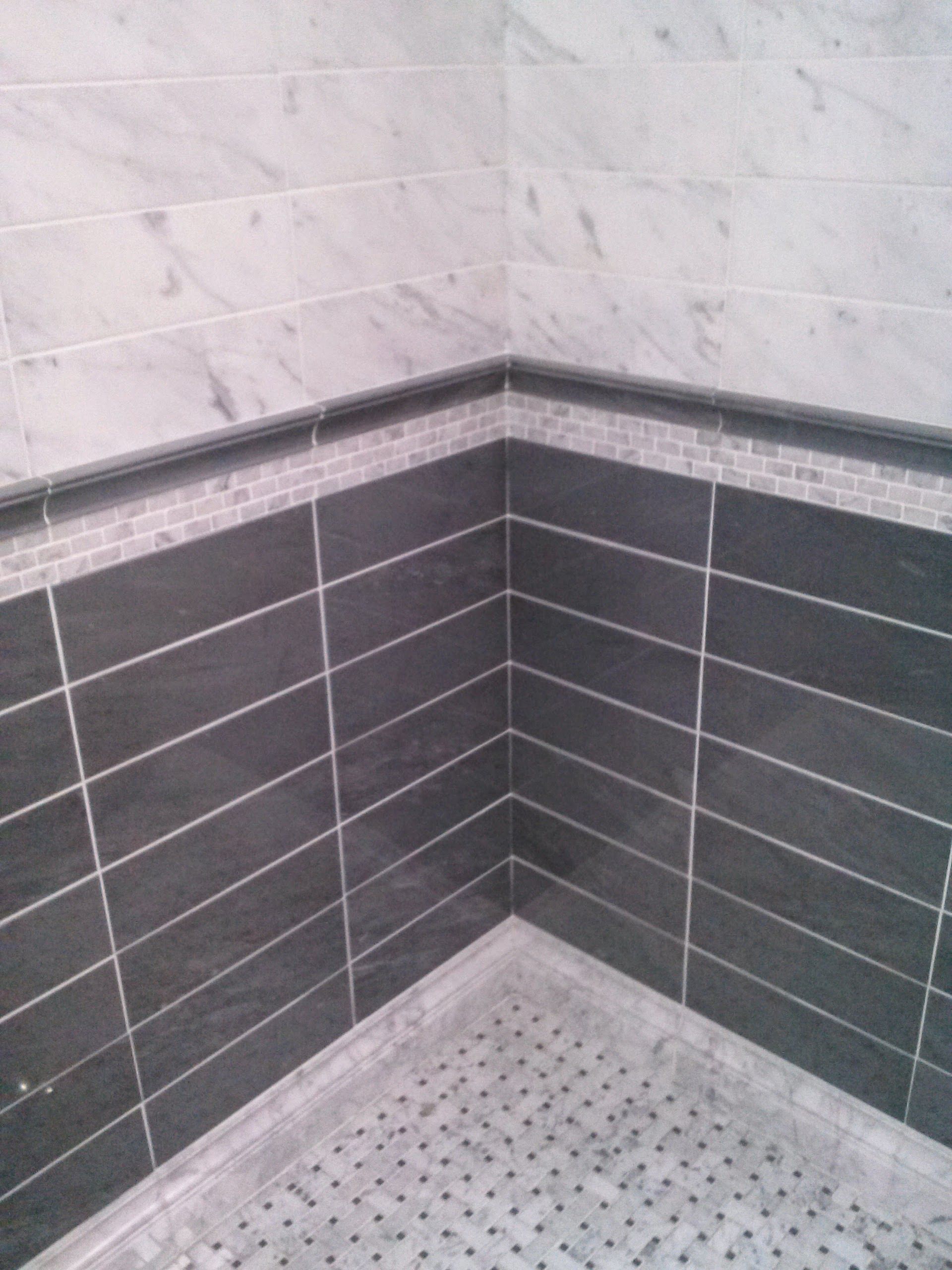 Shower corner with gray and white tiles and a mosaic border.