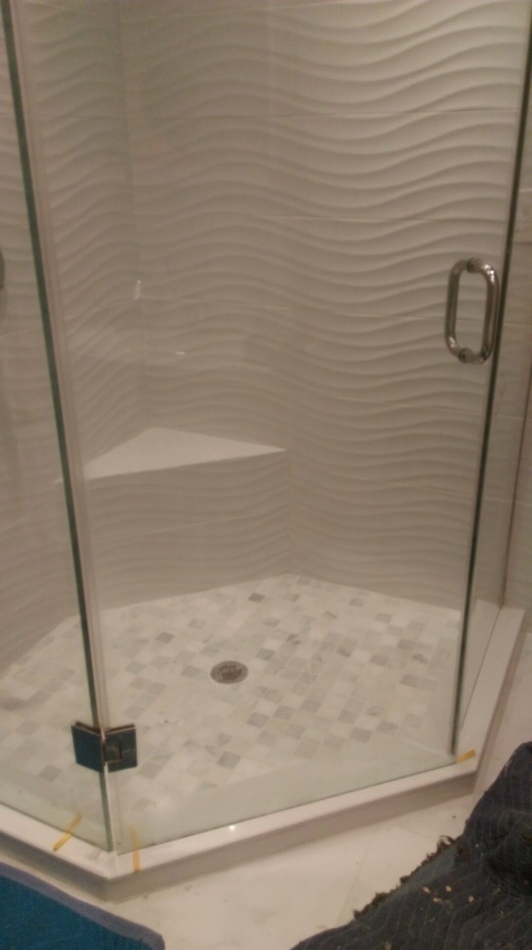 A glass shower with patterned tile floor, white wavy tile wall, and built-in corner shelf.