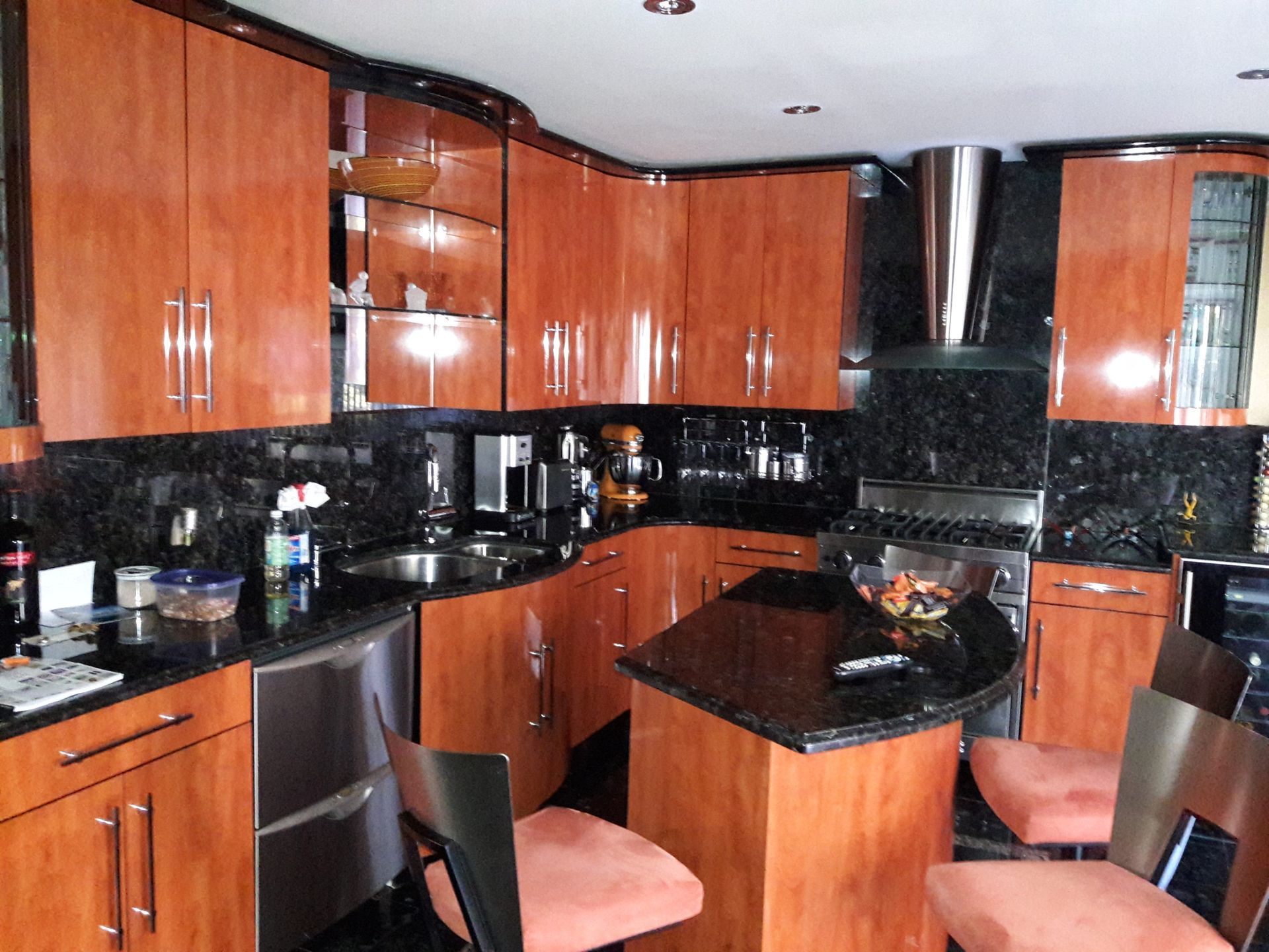 Kitchen with glossy orange cabinets, black countertops, and a small island with seating.