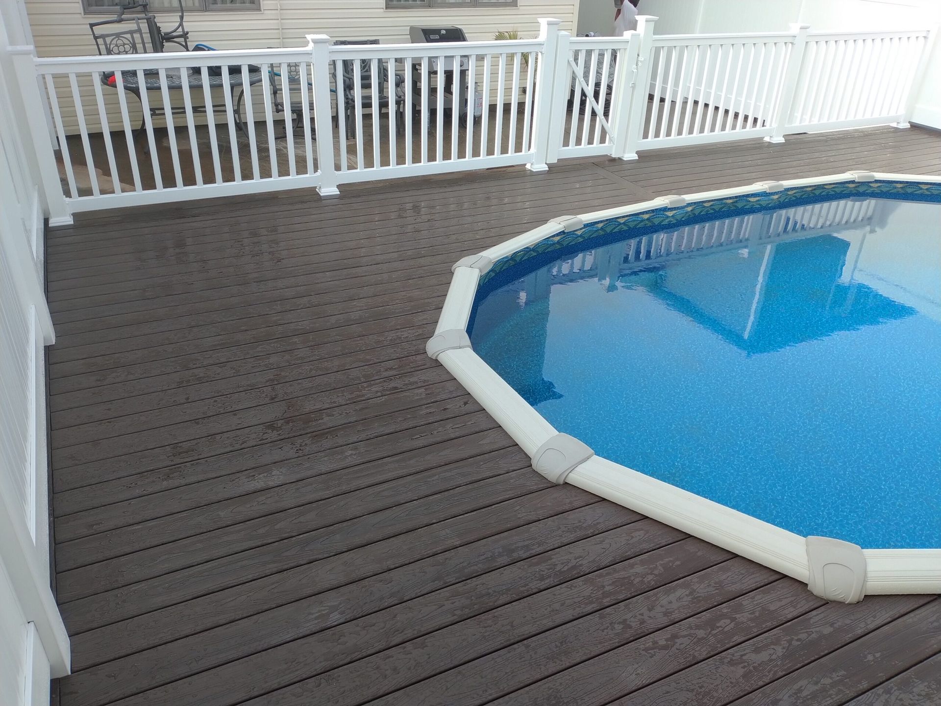 Brown composite deck surrounds an above-ground pool with white fencing.