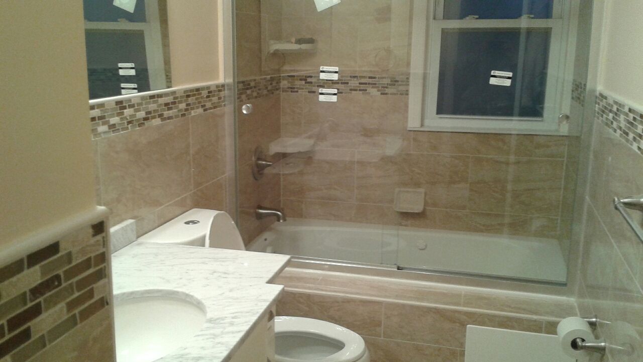 Bathroom with tiled walls, bathtub, toilet, vanity, and glass shower door.