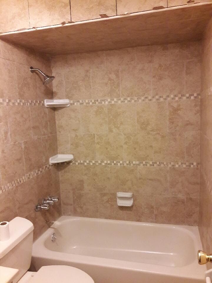 Beige-tiled shower stall with a white bathtub, soap dispensers, and a toilet.