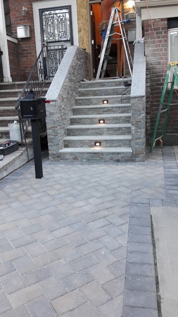 Brick home entrance with stone steps, embedded lights, and brick pavers. A ladder and tools are visible.