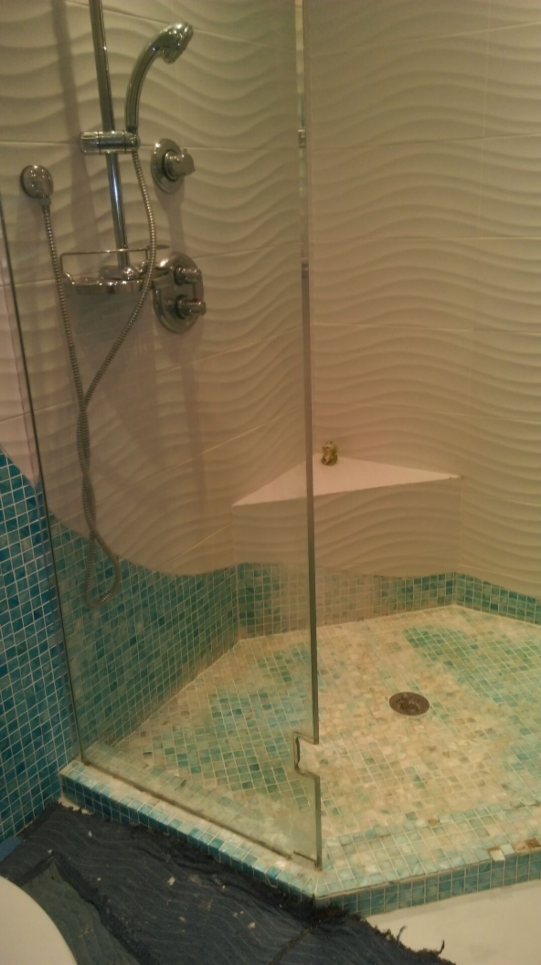 Shower stall with glass door, turquoise and white tile, and a built-in shelf.
