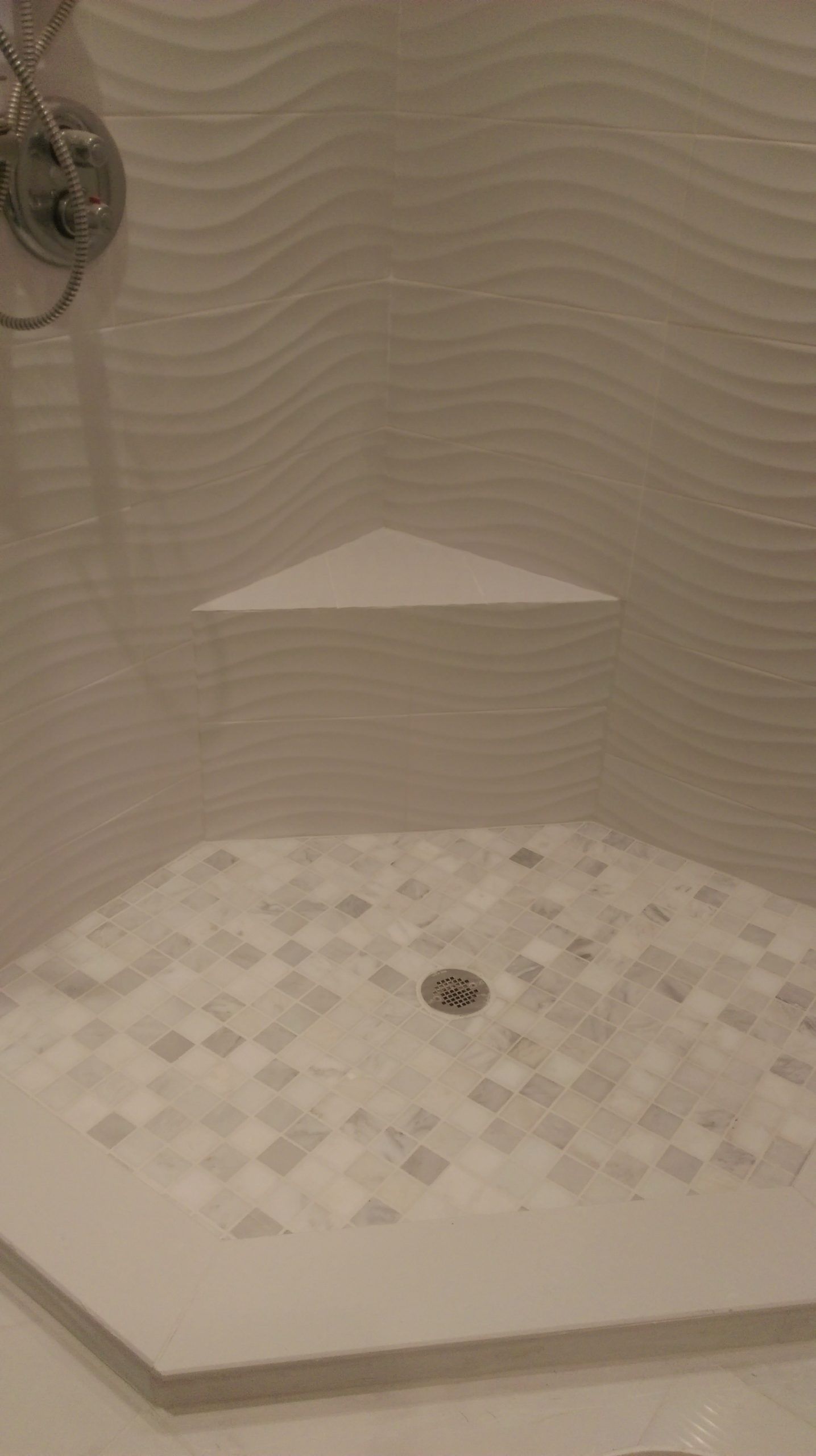 White tile shower with wavy wall tiles, a corner shelf, and mosaic floor.