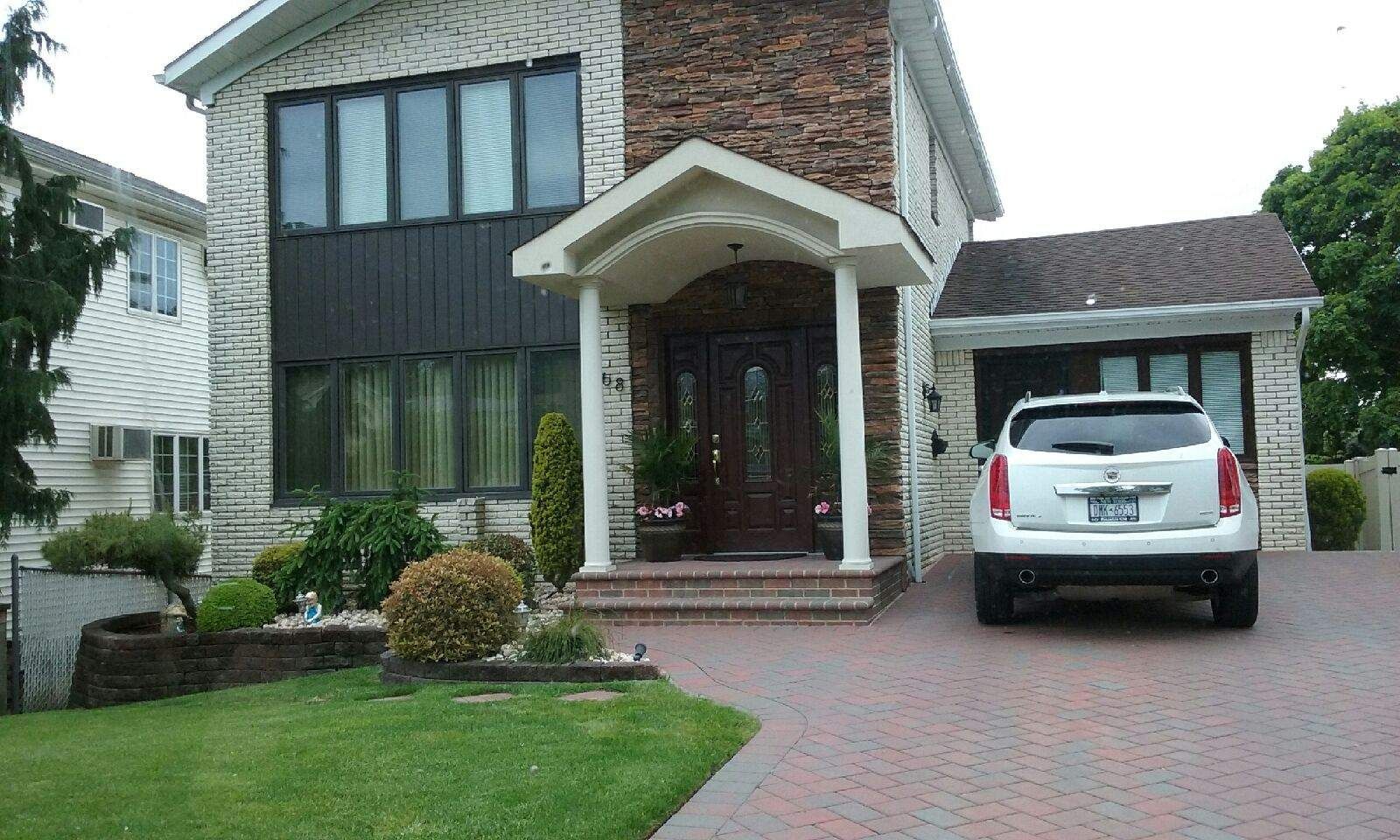 Two-story house with stone facade, dark wood door under a small portico. White SUV in driveway.