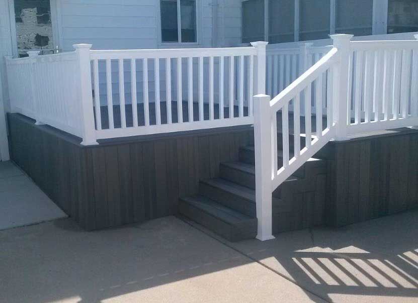 White fenced deck with steps against a light gray building; gray skirting.