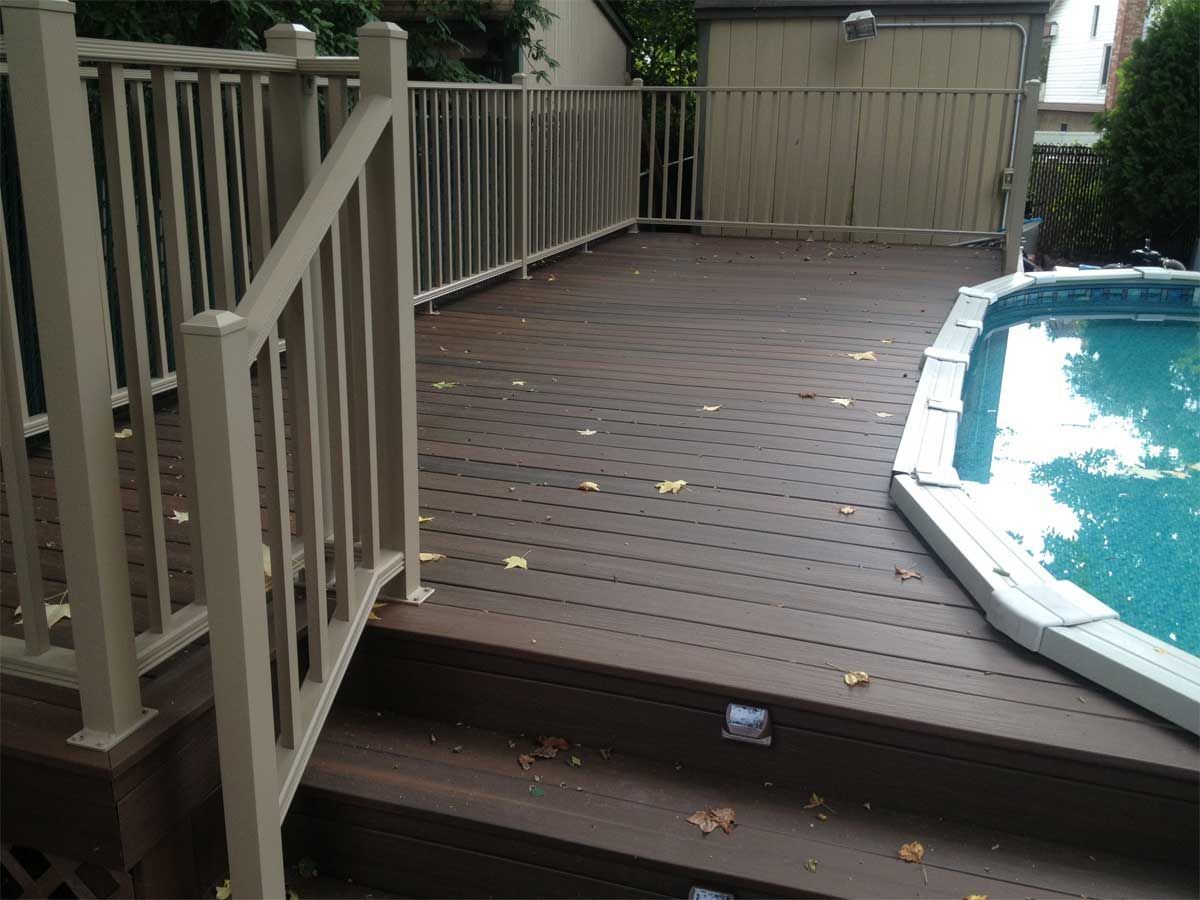 Brown deck with beige railing next to a pool. Steps lead down.