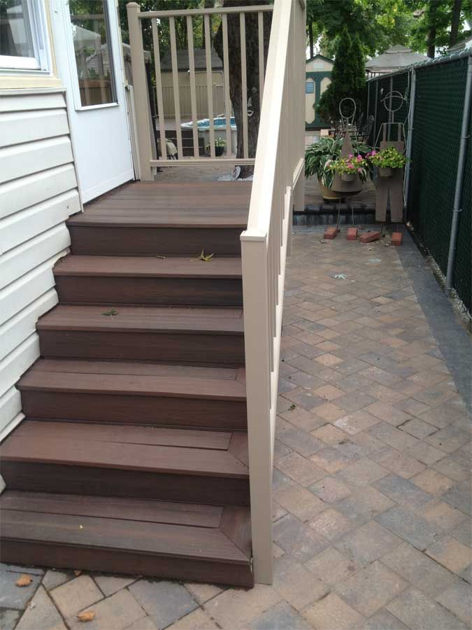 Wooden staircase leading to a back door and a brick patio. Beige handrails and side of building.
