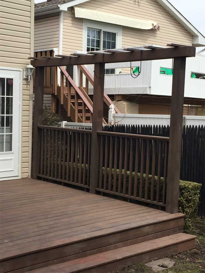Wooden deck with dark brown pergola and railing, tan house in background.