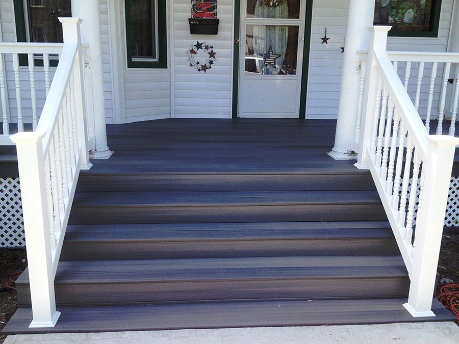 White-railed porch with dark gray steps and flooring leading to a white door; a wreath and mailbox are visible.