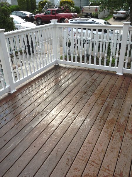 Wooden deck with white railing, wet surface, cars and houses in background.