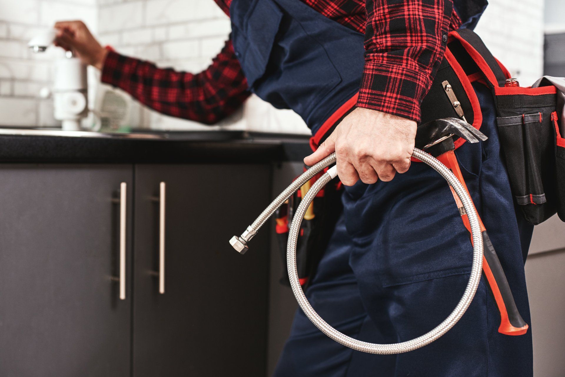 a plumber is holding a hose and a pair of pliers in a kitchen .