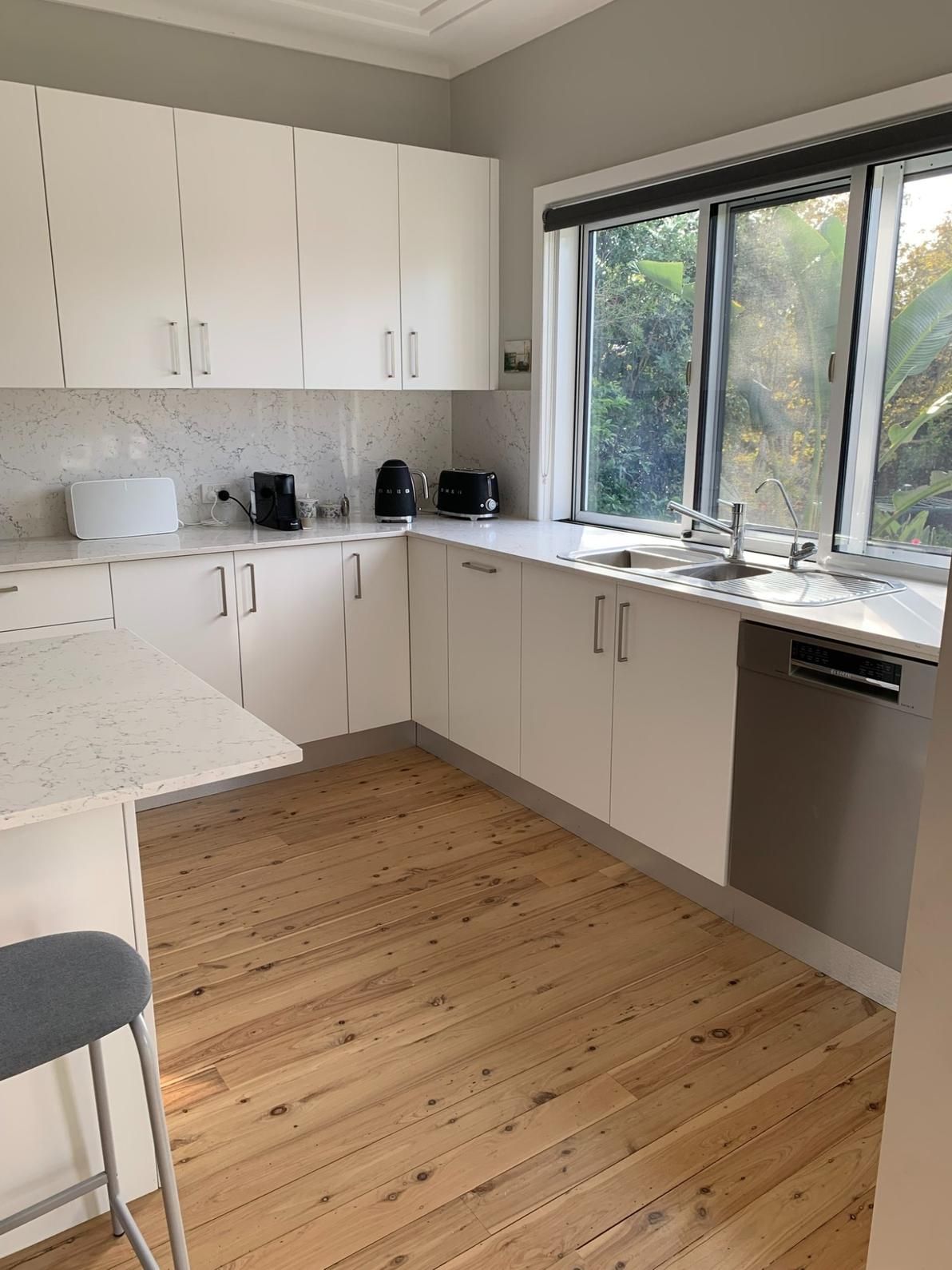 A Kitchen With White Cabinets and Wooden Floors and a Large Window — The Kitchen Centre In Erina, NSW